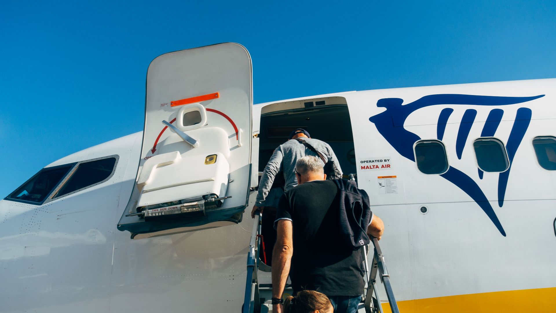 Travelers board a Ryanair plane for their flight under a clear blue sky.