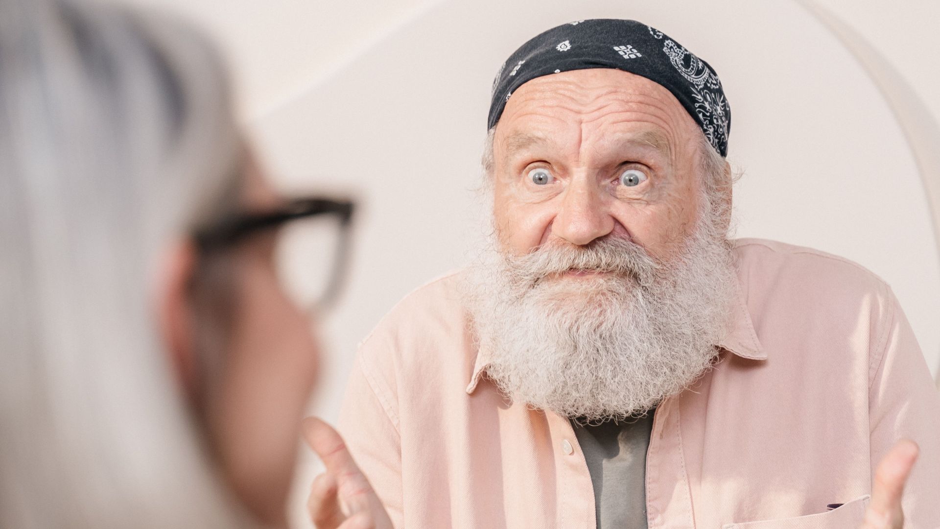 Elderly man animatedly discusses with a friend over coffee in a cozy indoor setting.