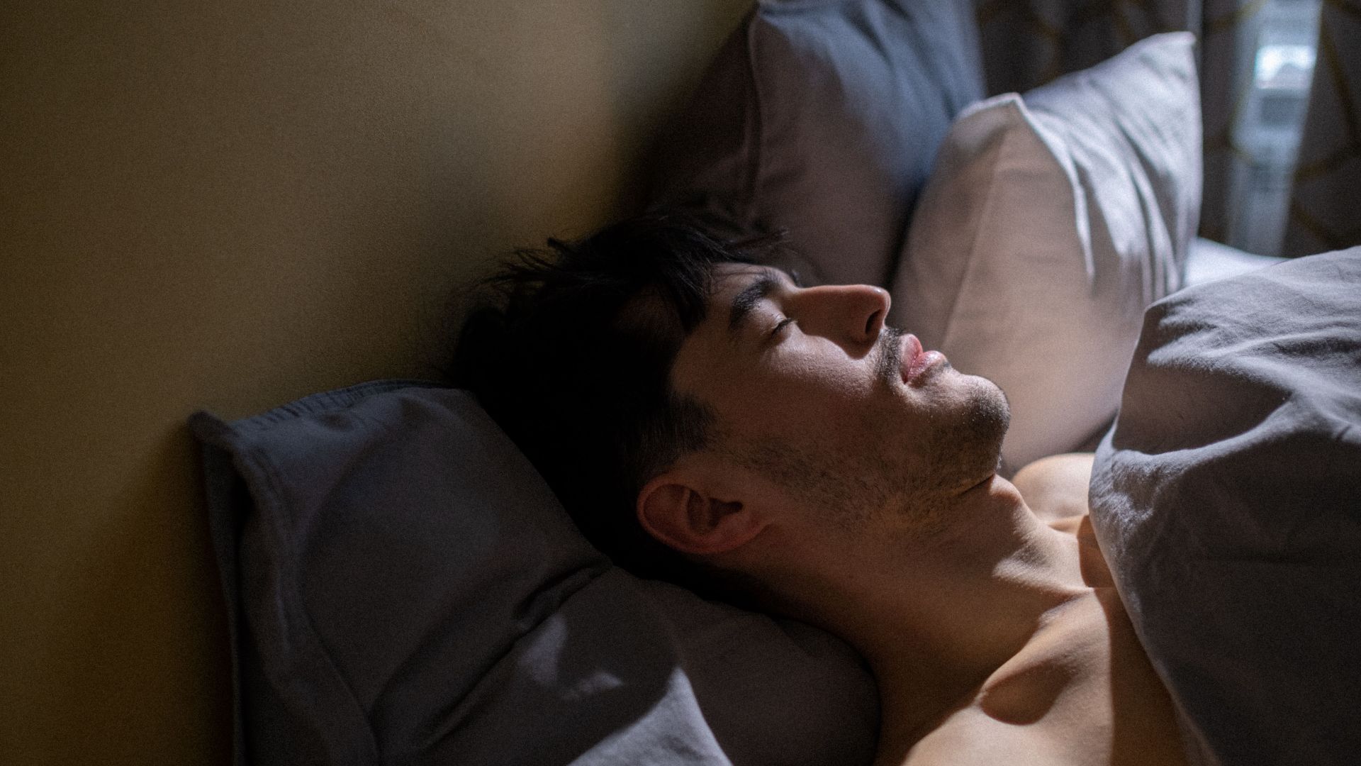 A man peacefully sleeping in bed with gentle morning light streaming in a cozy bedroom.
