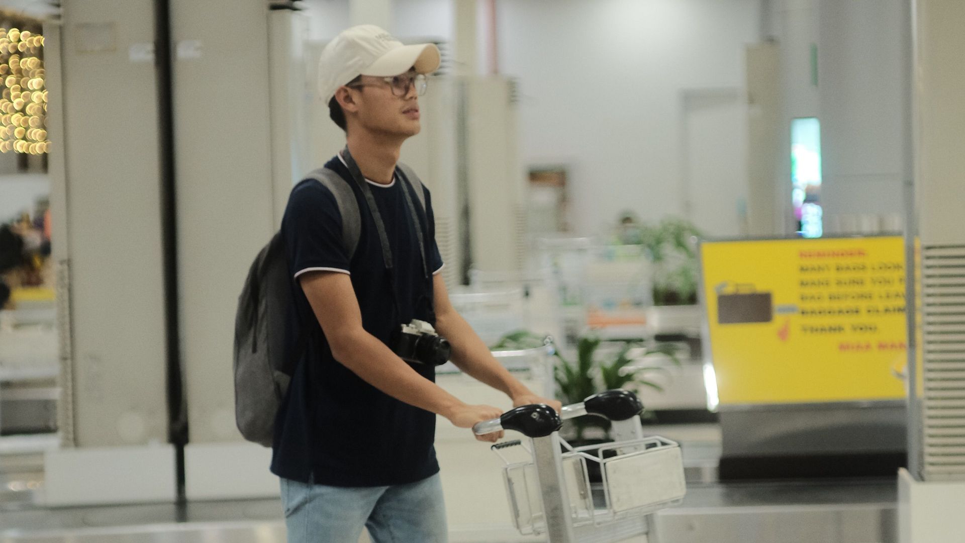A young man pushes a luggage cart in an airport baggage claim area.