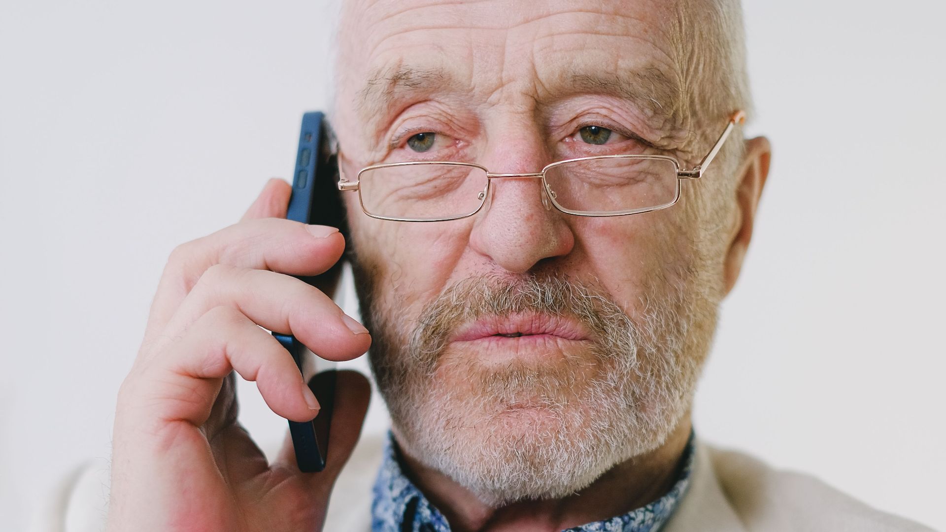 Portrait of a senior Caucasian man with eyeglasses talking on a smartphone indoors.