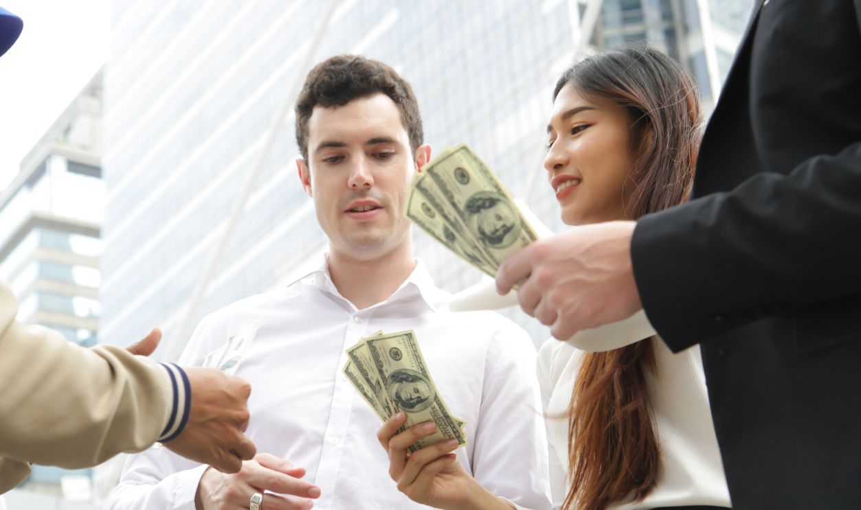 Shutterstock-1203993637, business partners showing money to exchange. holding US dollar, offers dollar bank note. cash in business, Paying compensation to partners.