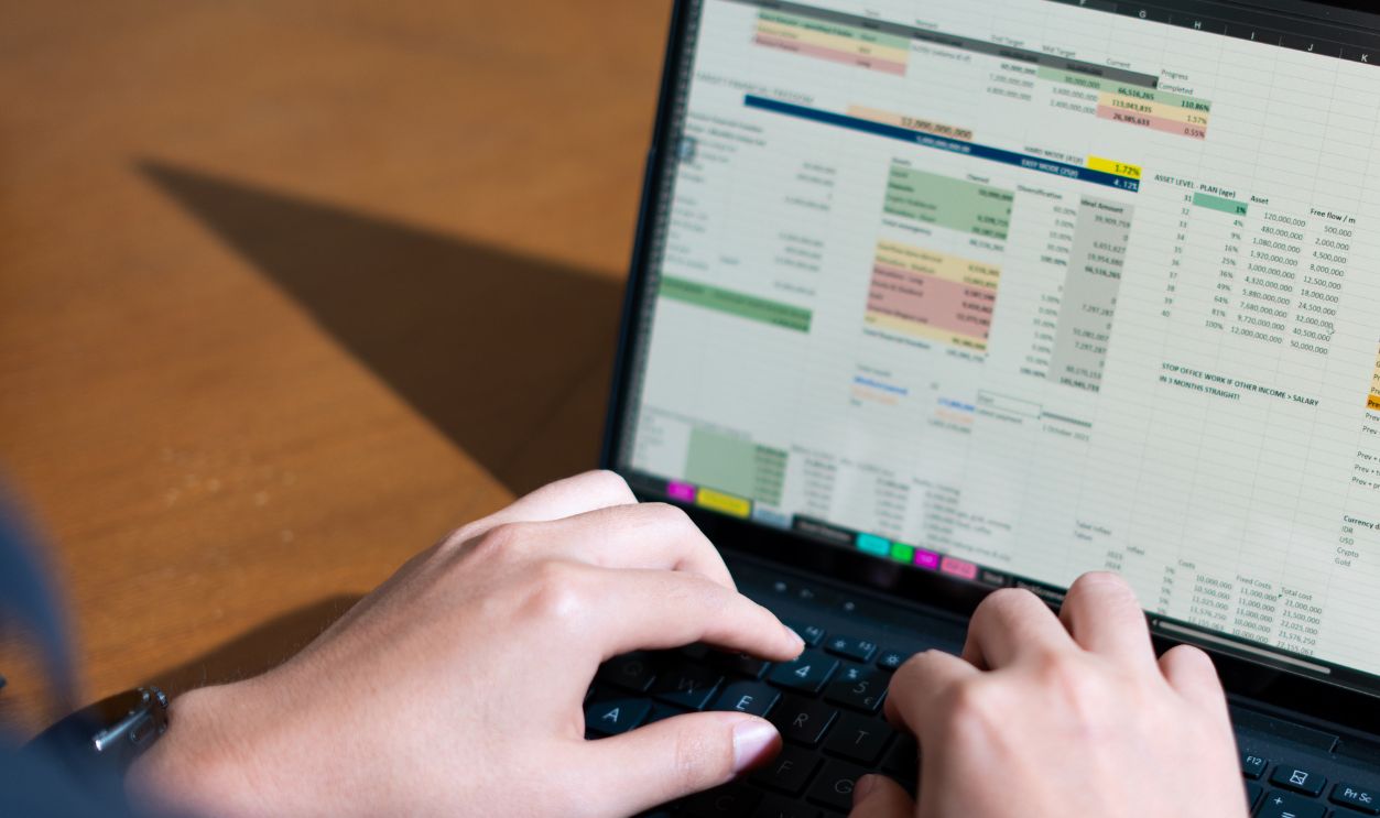 Over-the-shoulder shot of a person managing personal finances using a budgeting app spreadsheet on a clean workspace.