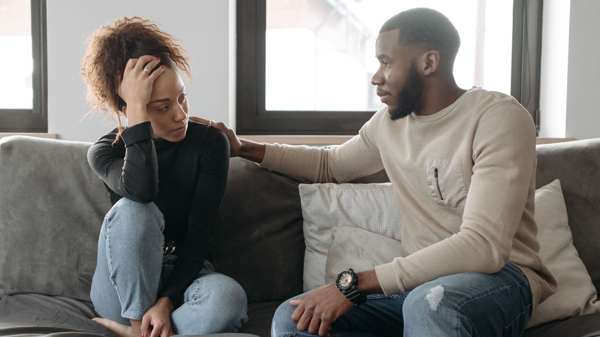 A couple shares a moment on their sofa at home, conveying care and understanding.