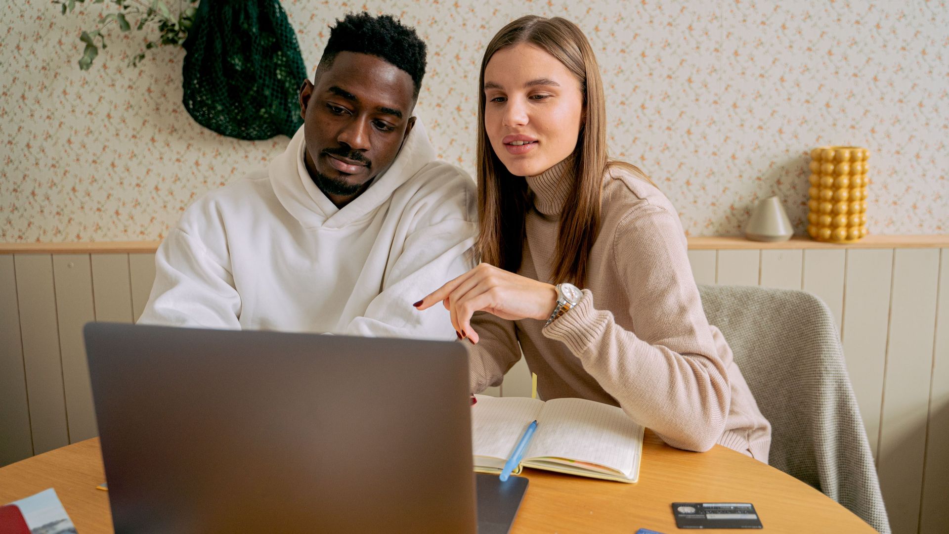 An interracial couple engaged in collaborative work on a laptop indoors, fostering teamwork.