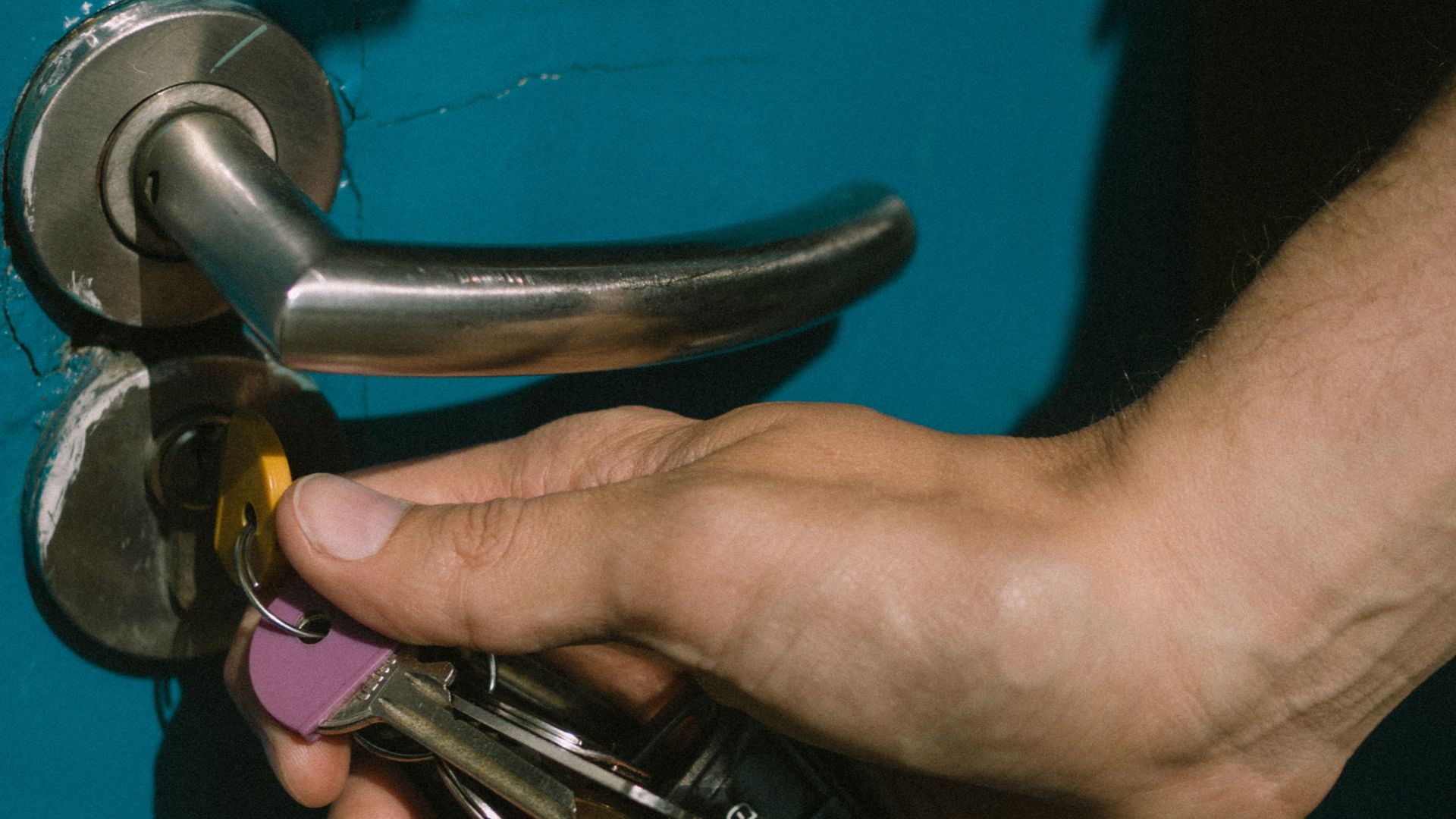 A hand using keys to unlock a vibrant blue door with a metal handle.