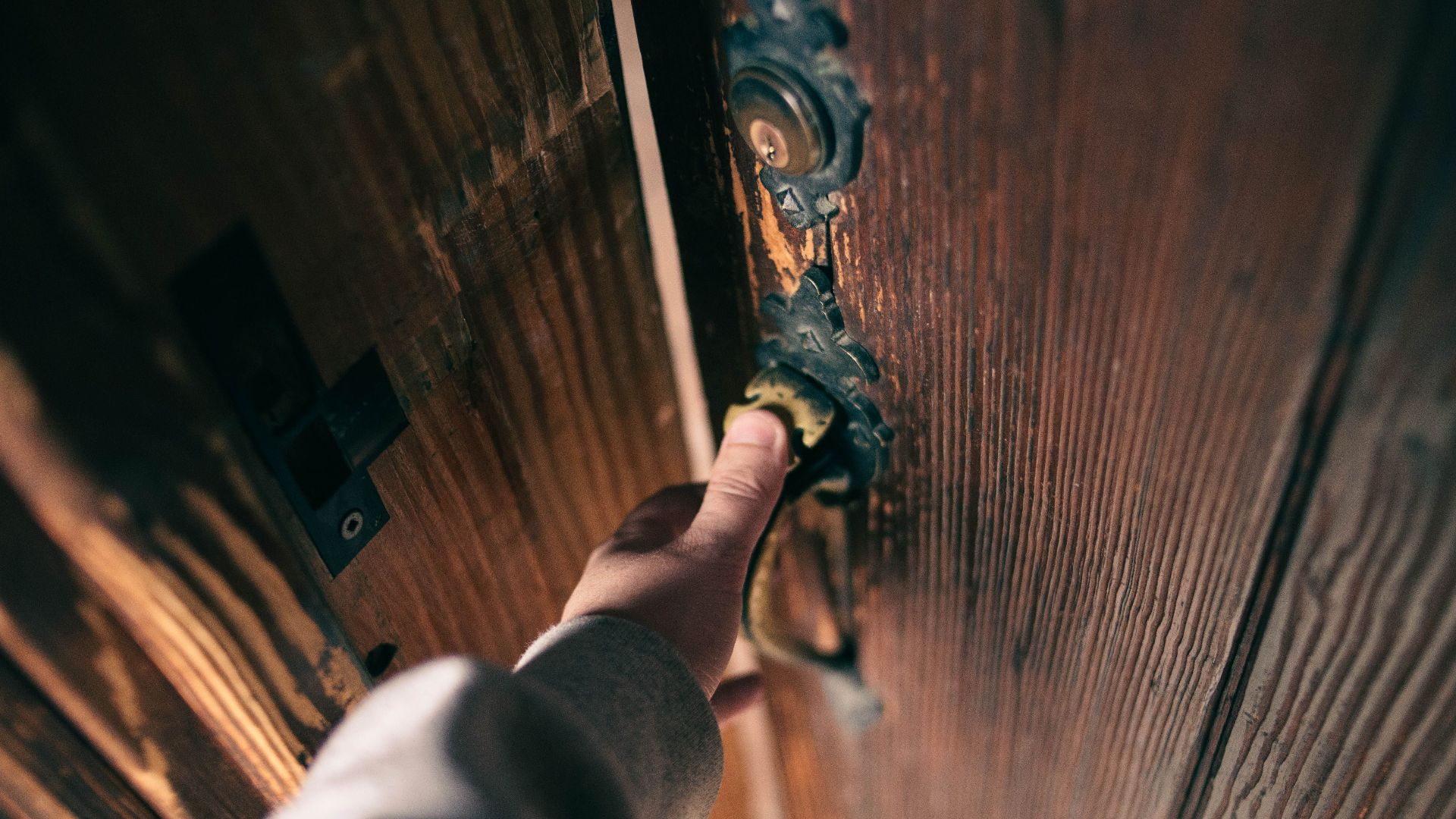 Close-up view of a hand opening a vintage wooden door with ornate handle, creating a warm and inviting atmosphere.