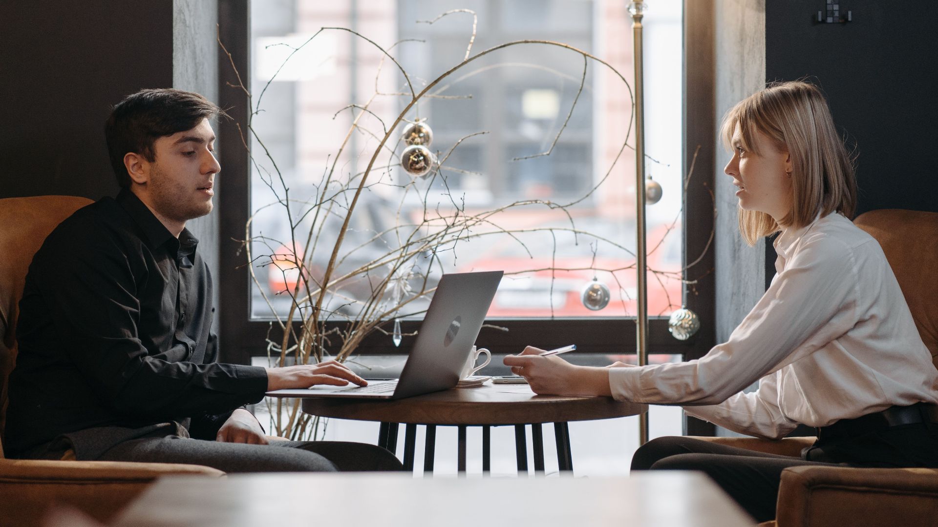 A young man and woman engaged in a business meeting with a laptop in a cozy cafe.