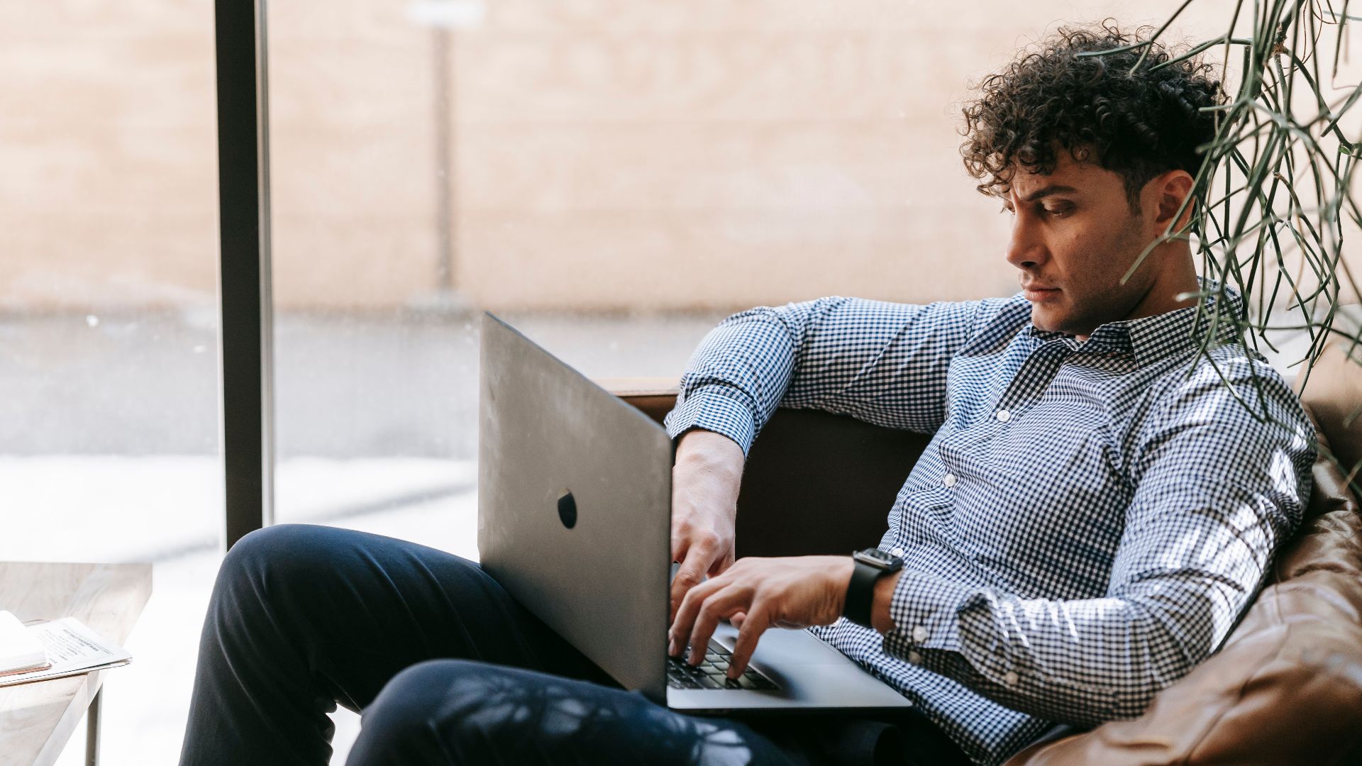 A man in smart casual attire using a laptop on a couch indoors.