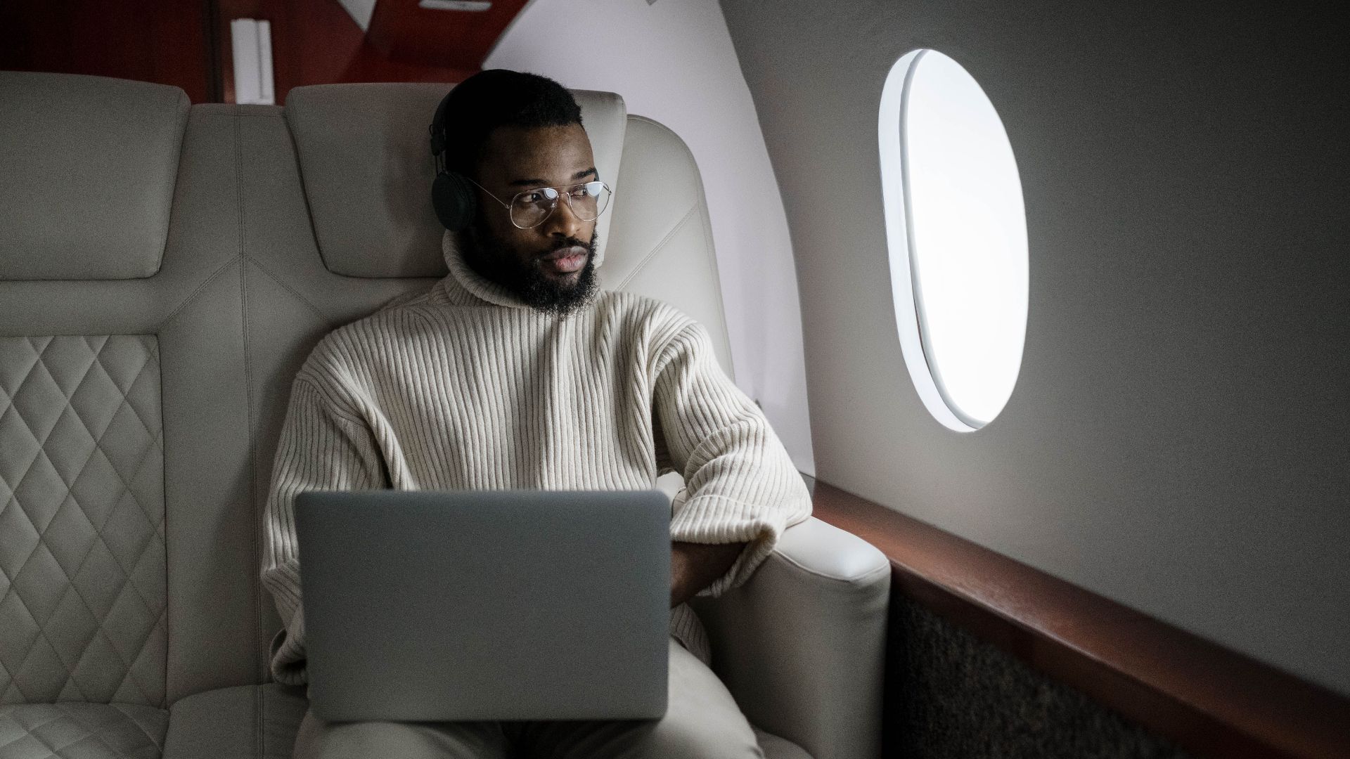 A man wearing headphones uses a laptop in a luxurious airplane cabin.