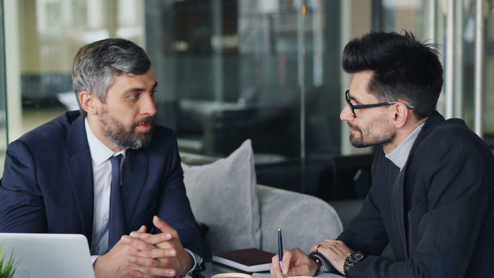 Two businessmen having a meeting with laptops, papers, and coffee at a modern office.
