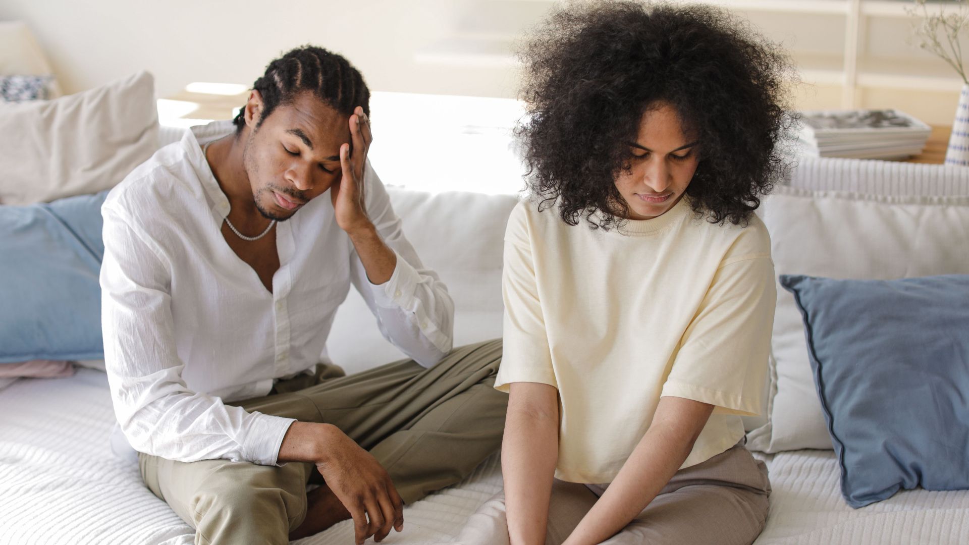 A contemplative black couple sitting on a sofa indoors in a modern setting, reflecting emotions.
