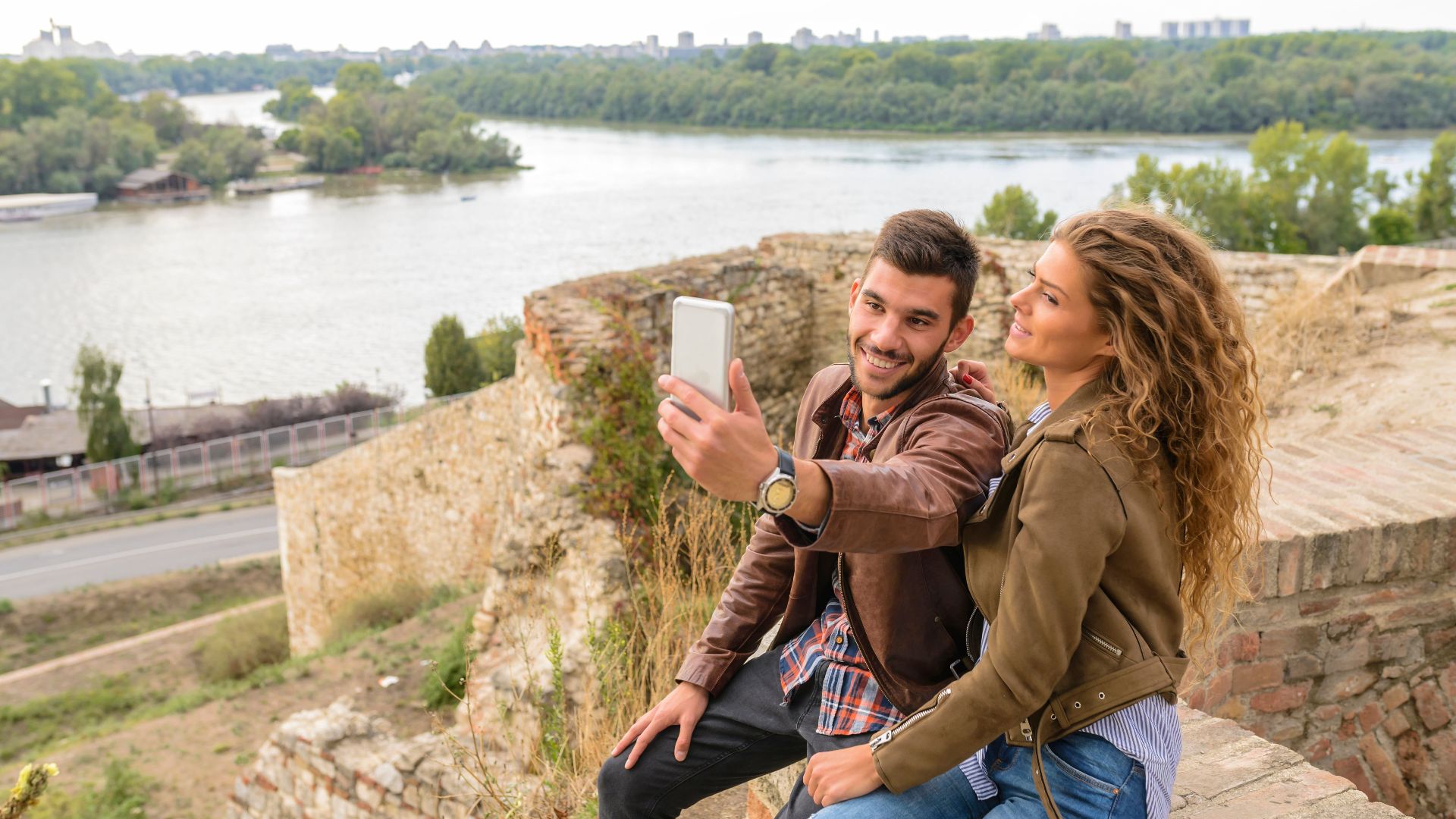 Happy couple takes a selfie at a scenic riverside location, enjoying their time outdoors.