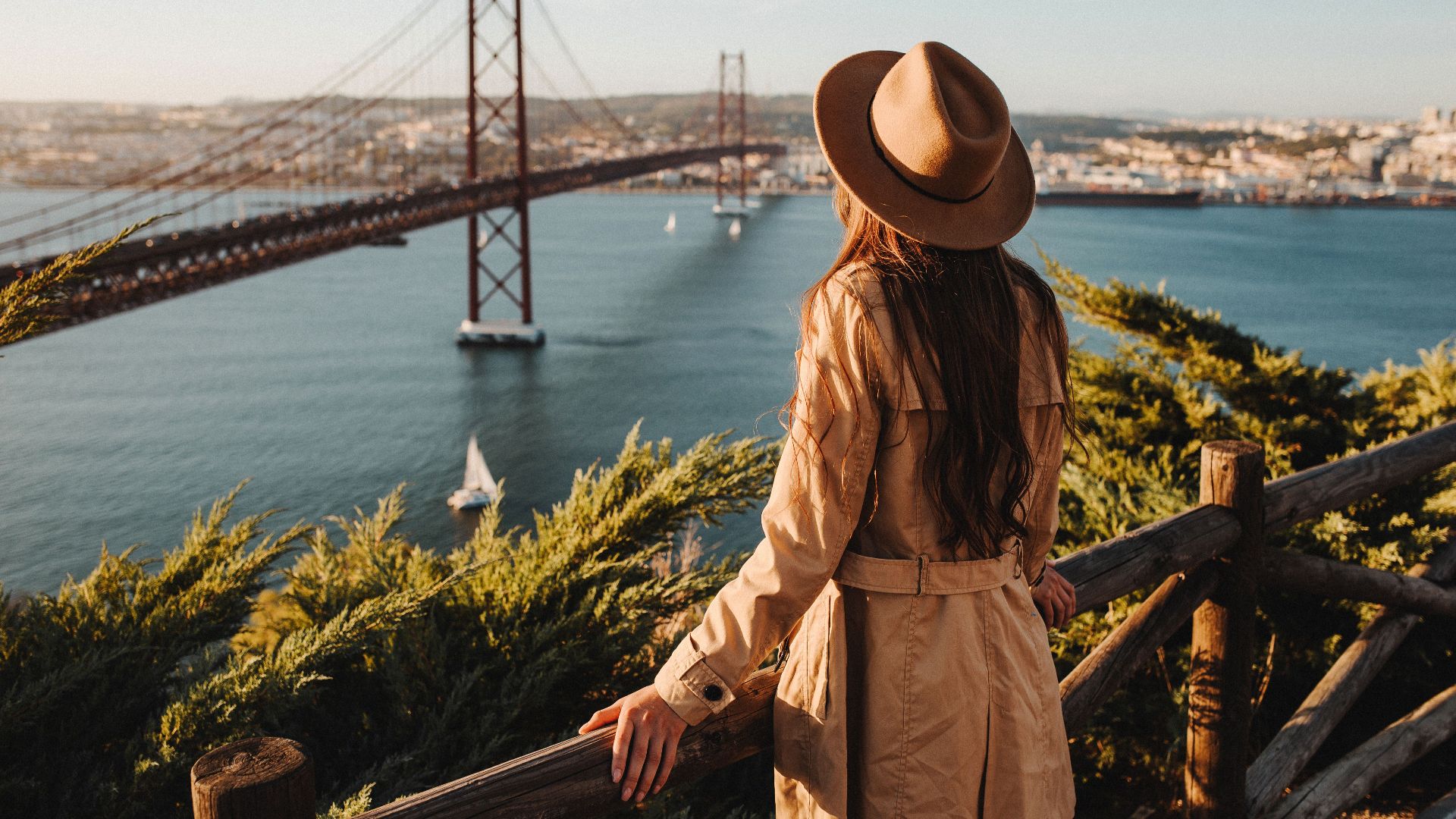 A woman in a hat overlooks the 25 de Abril Bridge in Lisbon, Portugal.