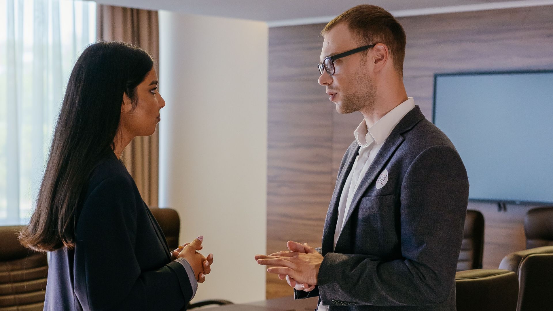 Two professionals engaged in discussion inside a modern conference room setting.