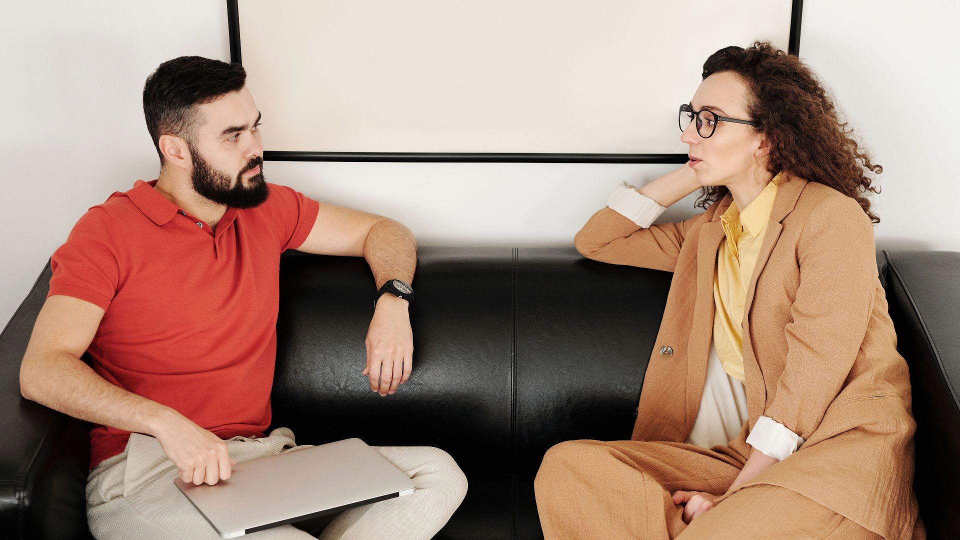 A man and woman sit on a black sofa, having a professional conversation.