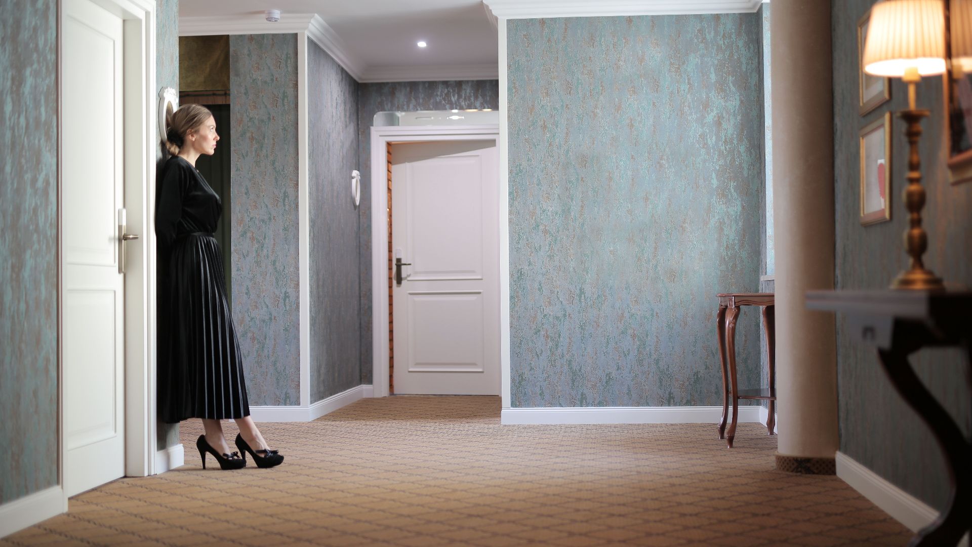 Elegant hotel hallway with a woman in a black dress leaning against a door.