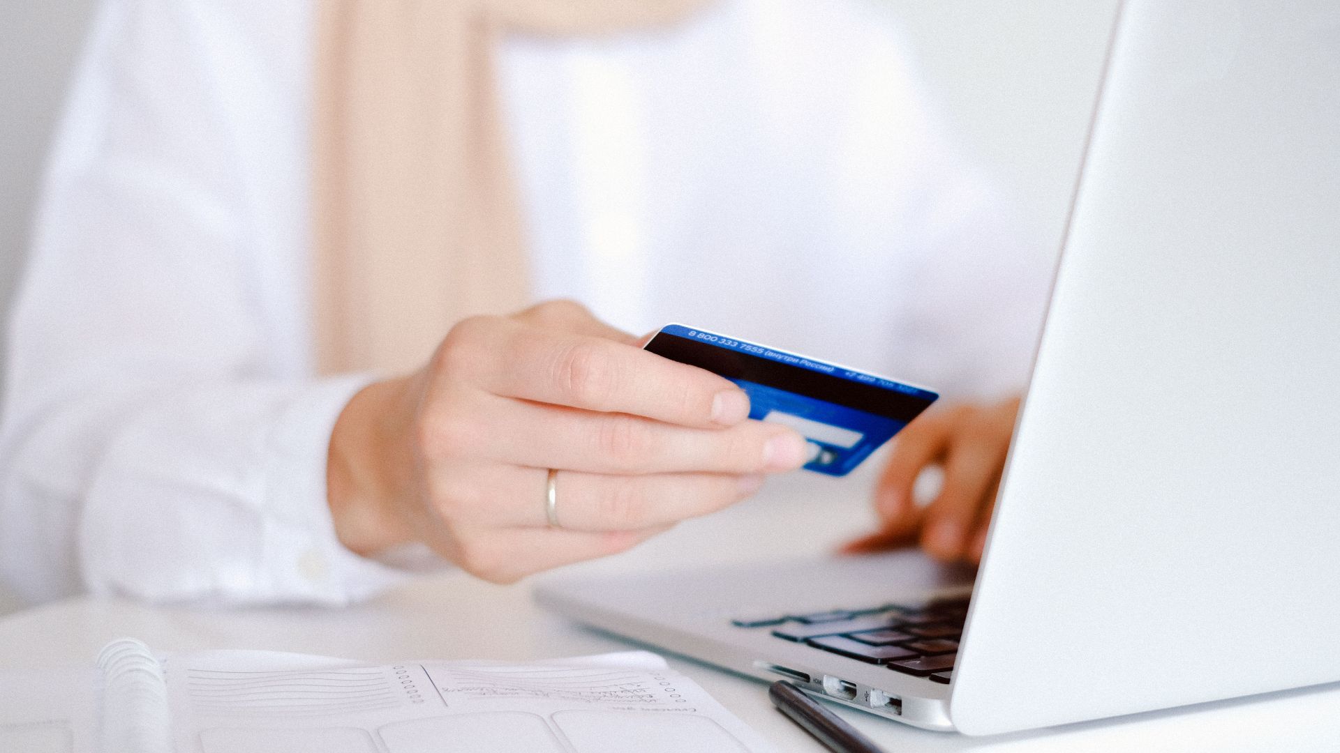 Close-up of a person holding a credit card while using a laptop for online shopping.