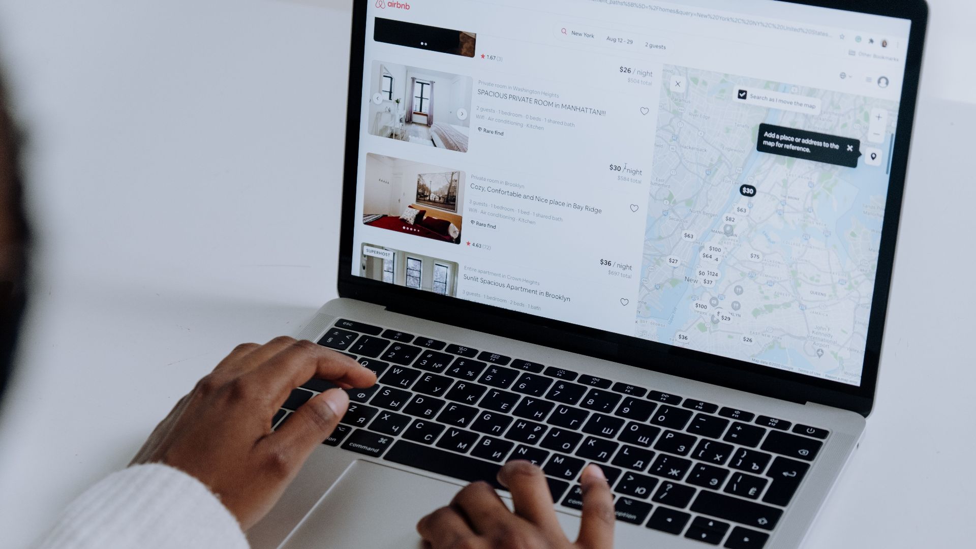 Hands typing on laptop searching Airbnb for accommodation options with map view.