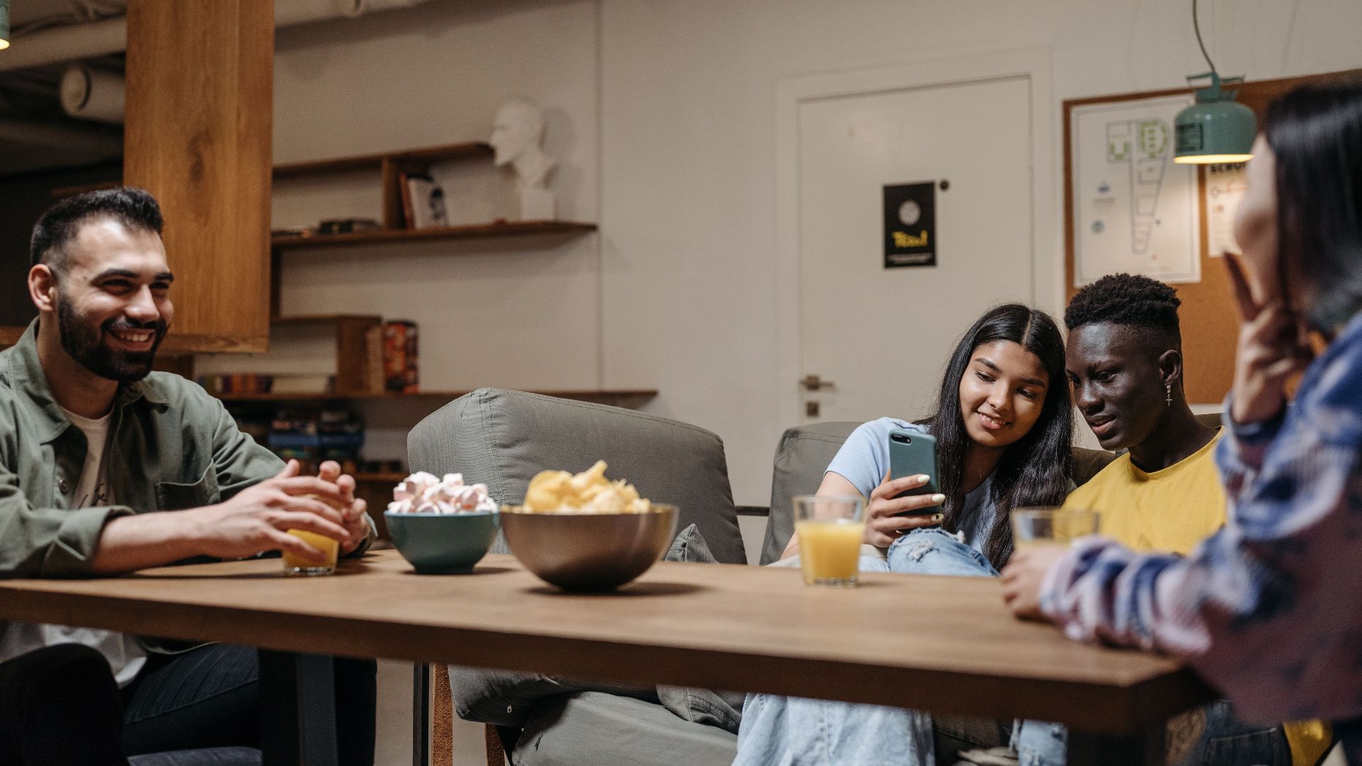 A diverse group of friends sitting together enjoying snacks and drinks indoors, capturing a moment of relaxation and bonding.