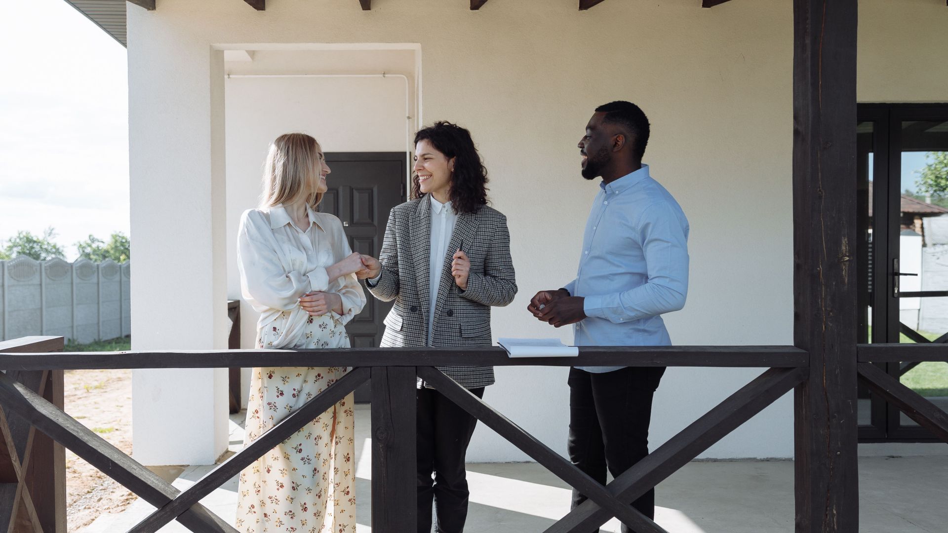 A real estate agent discussing property details with clients on a sunny porch.