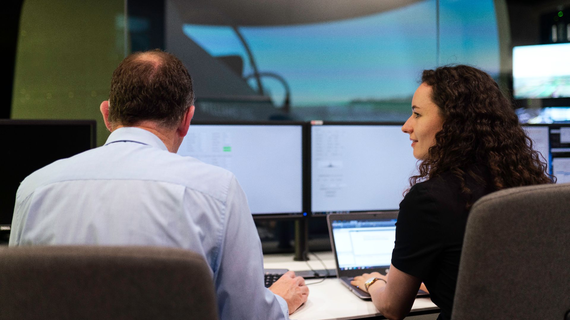 Two engineers working together on a computer simulation in a control room.