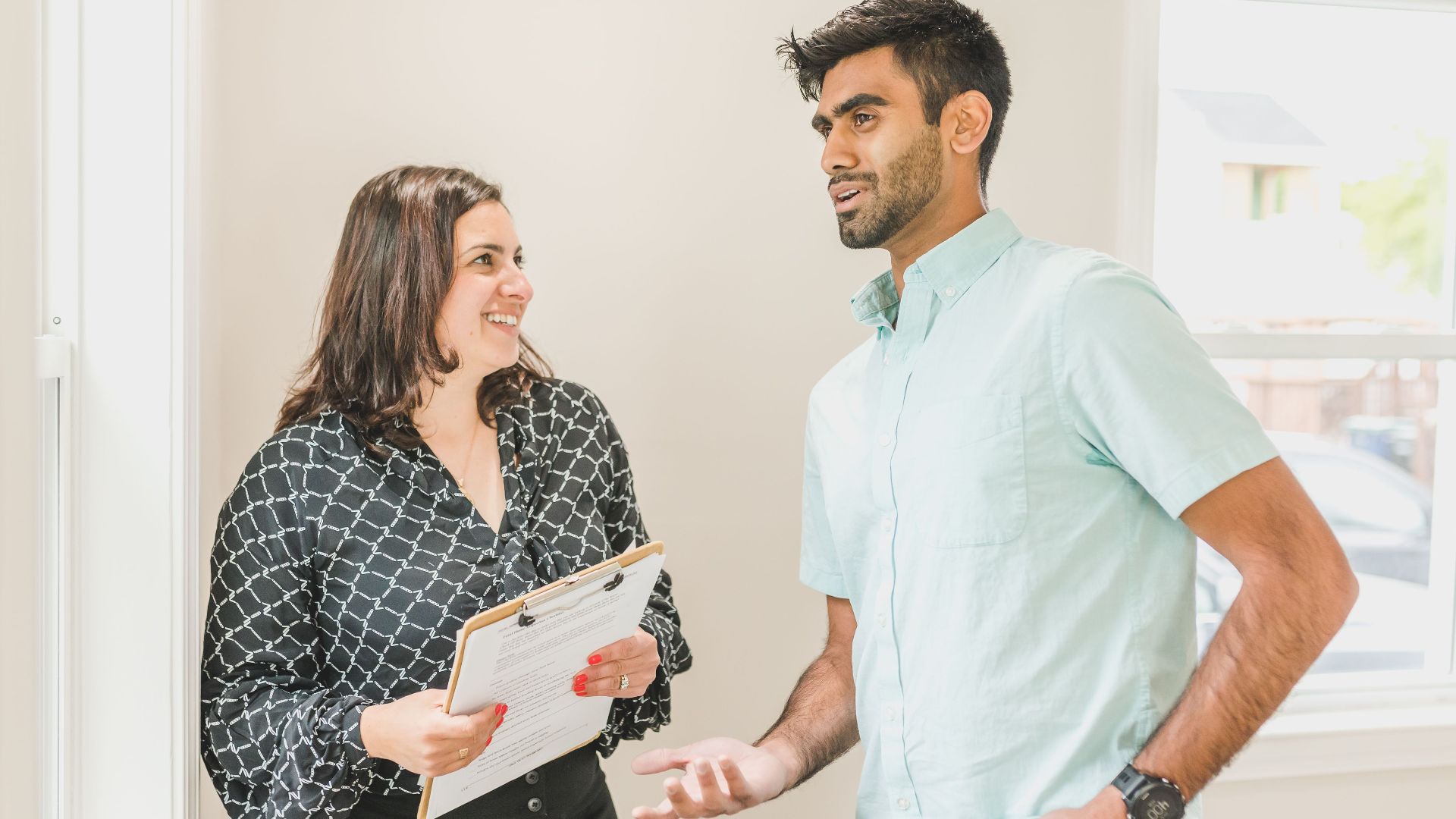 Real estate agent smiles while discussing property details with a client indoors.