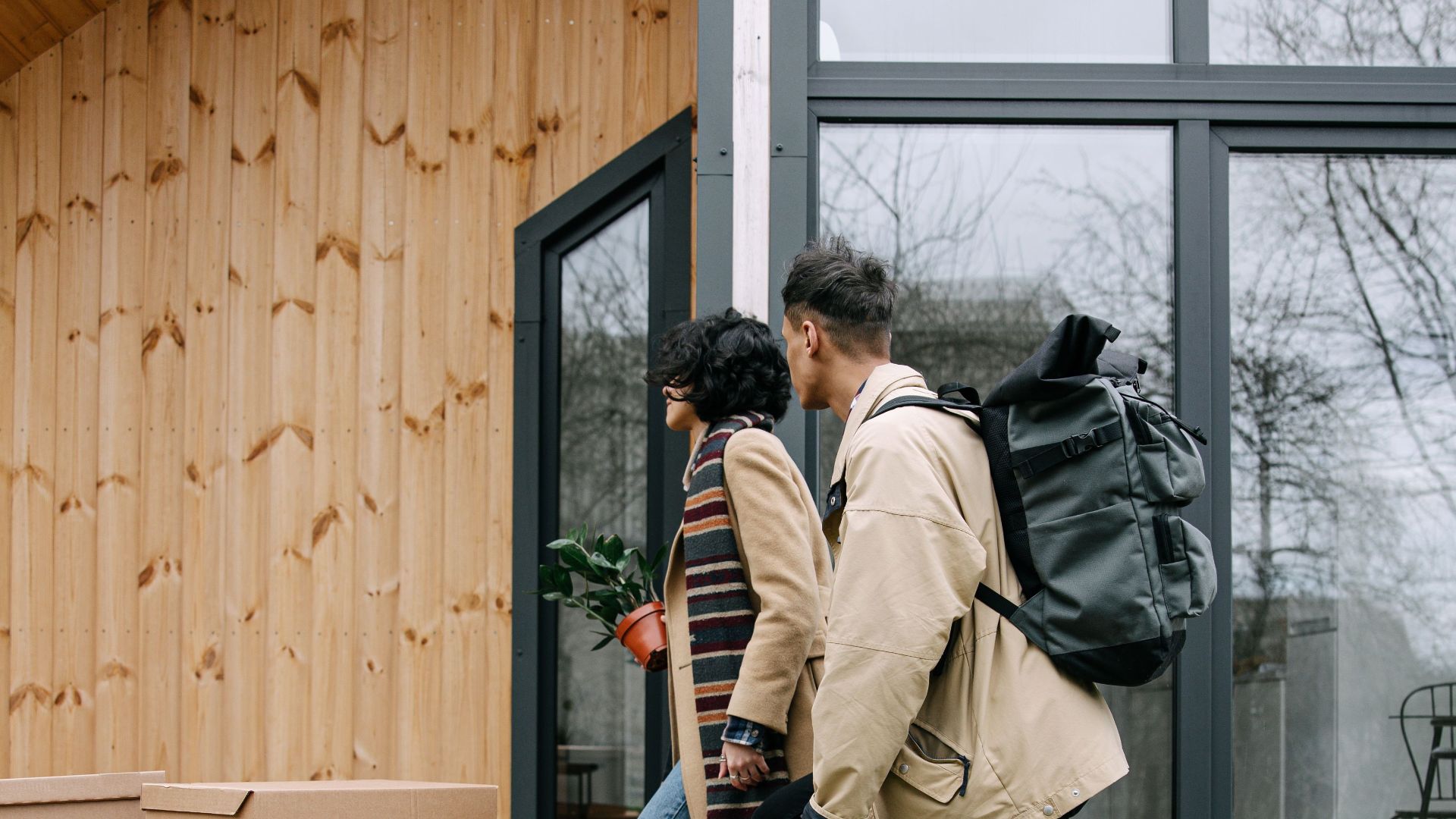 A couple moving boxes into their new wooden house on a sunny day.