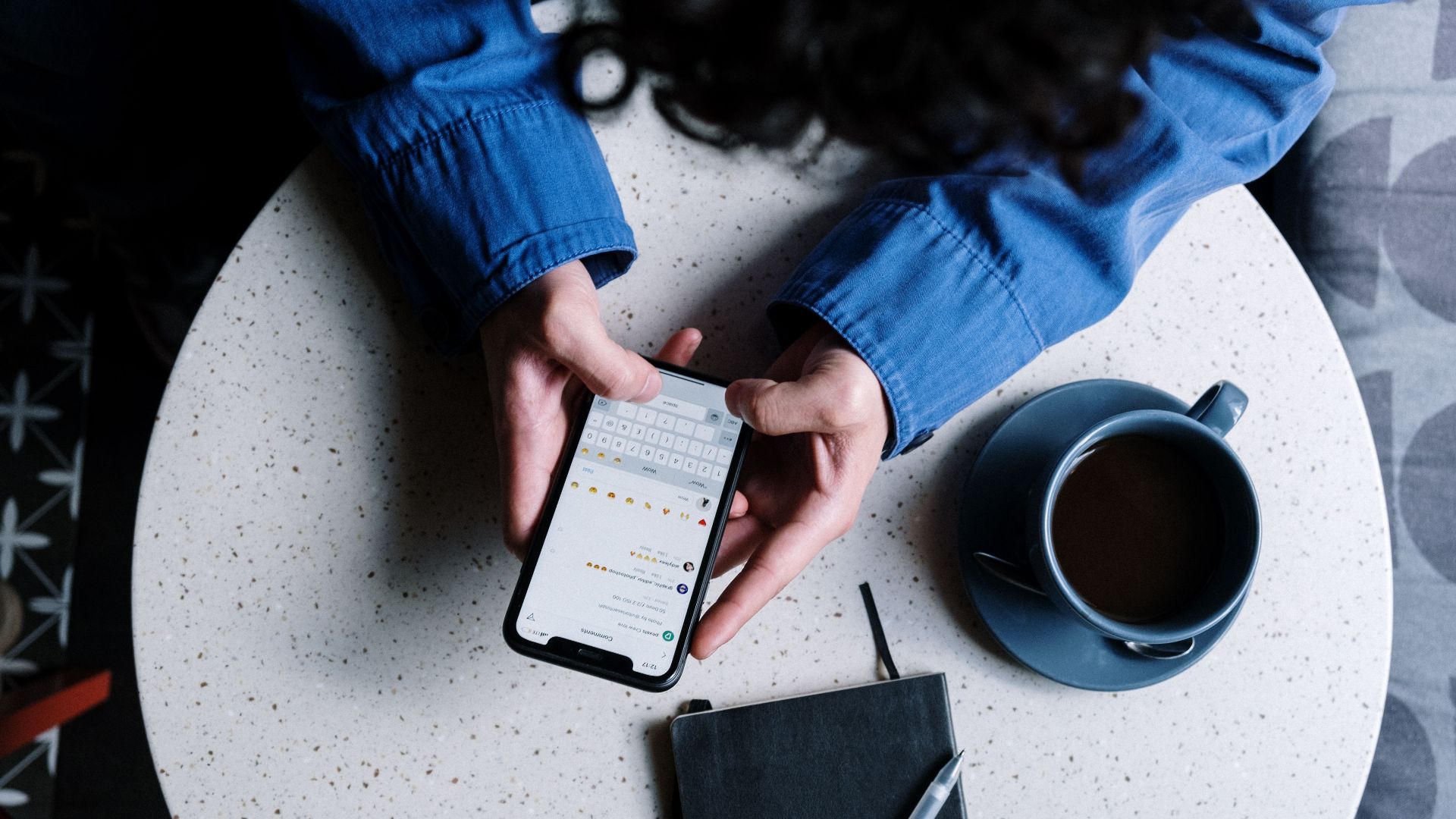 Person using smartphone at table with notebook and coffee, ideal for tech and lifestyle themes.