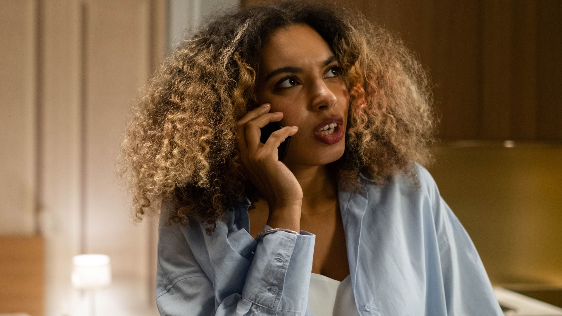 Adult woman with curly hair making a phone call indoors, lifestyle scene.