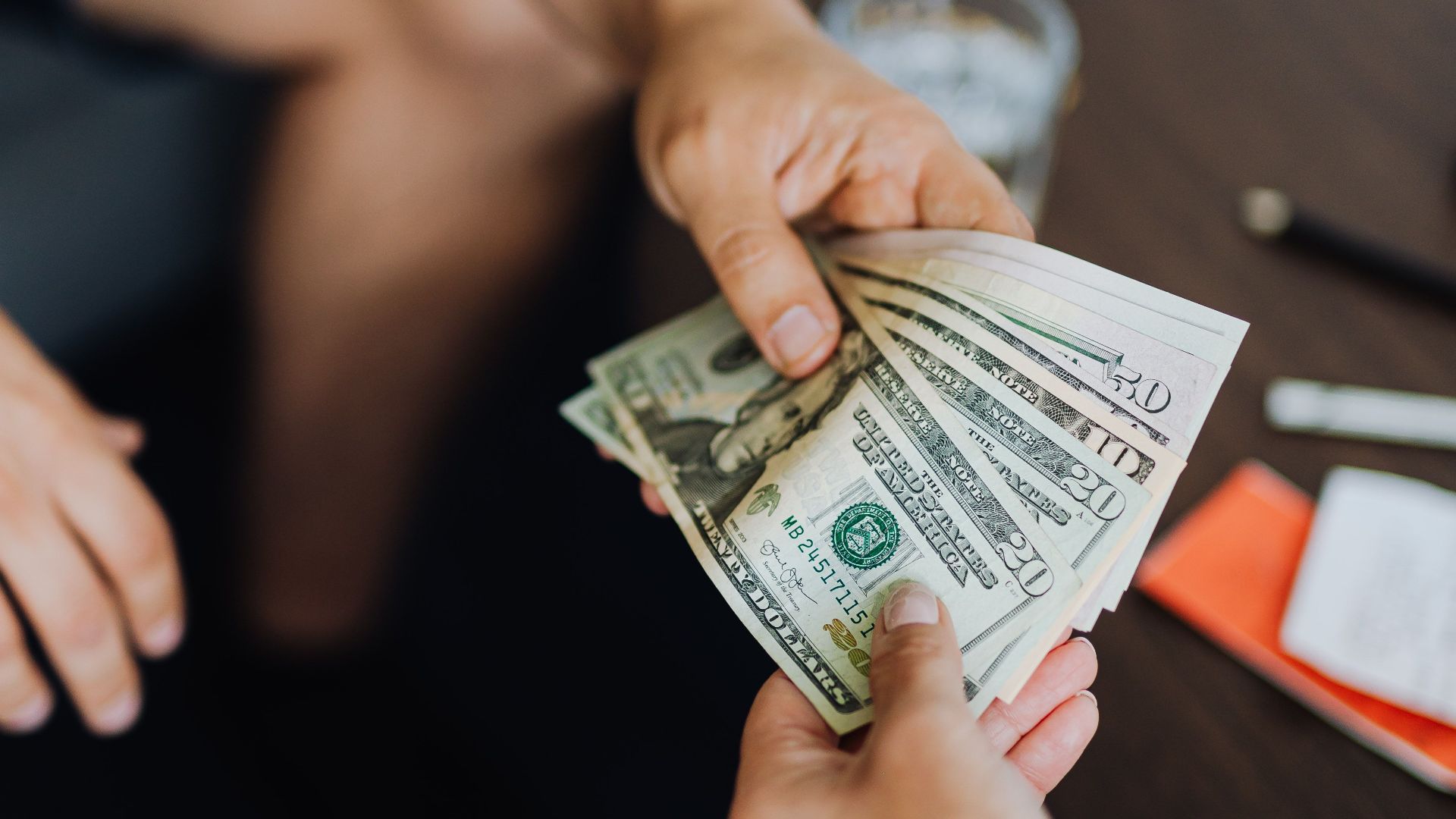 A close-up view of hands exchanging dollar bills indoors, symbolizing payment.