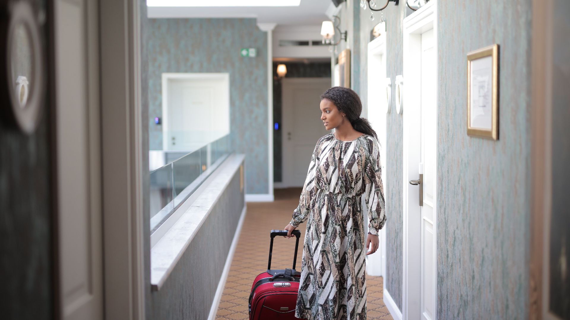 A woman walks with luggage through a stylish hotel corridor, embodying travel elegance.