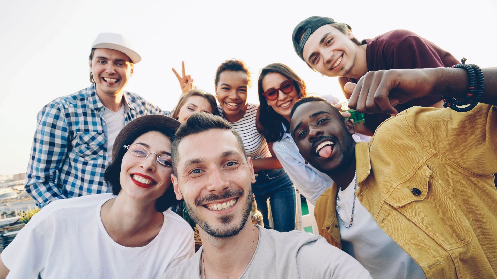 A diverse group of friends smiles while taking a selfie outdoors during the day.