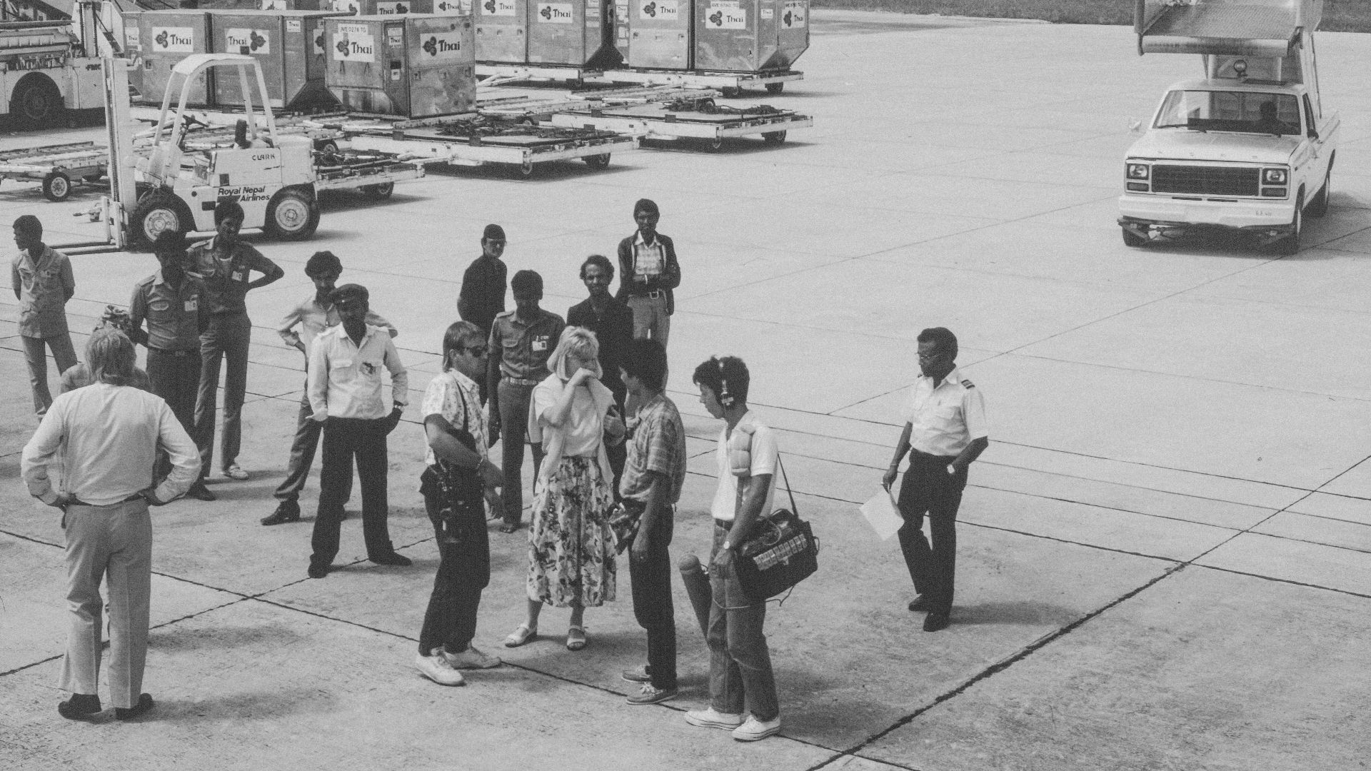 People gathered on an airport tarmac with luggage and vehicles