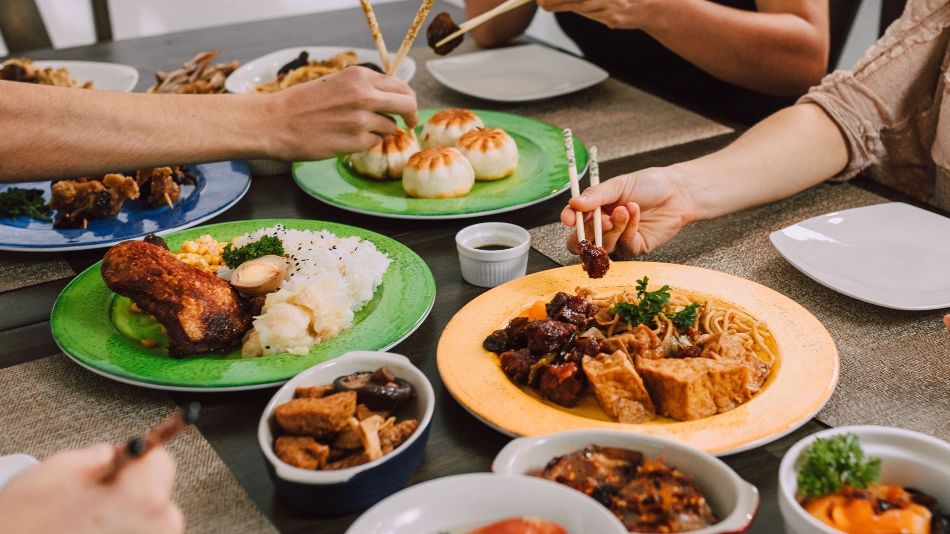 Diners enjoy a variety of Asian dishes including buns, noodles, and rice at a shared table.