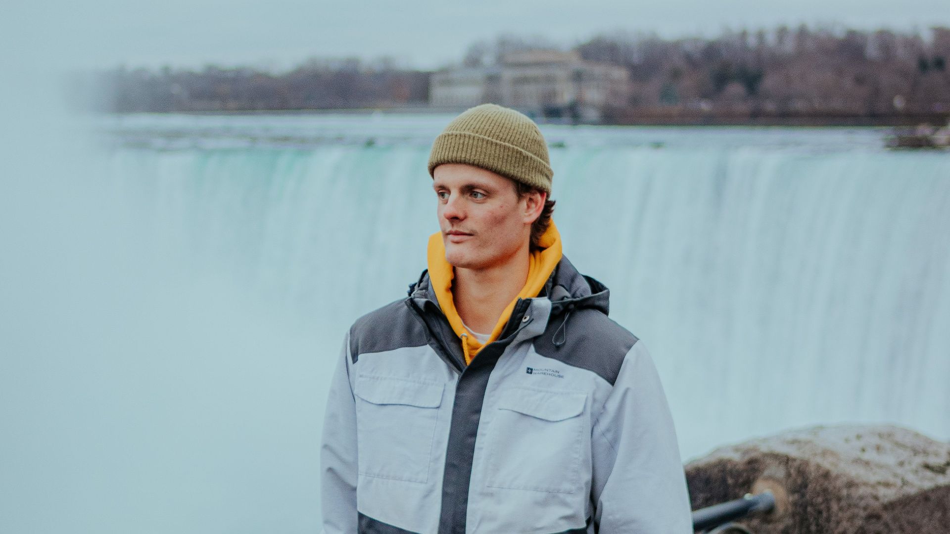 Caucasian man in a jacket at Niagara Falls, showcasing nature's beauty on a cloudy day.