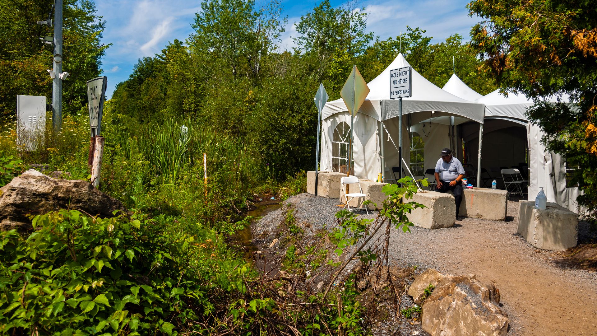 Looking west along the US-Canadian border vista at Roxham Road, Champlain, NY. US side is on left; tents on right are set up to handle asylum seekers from US who have been crossing here illegally.