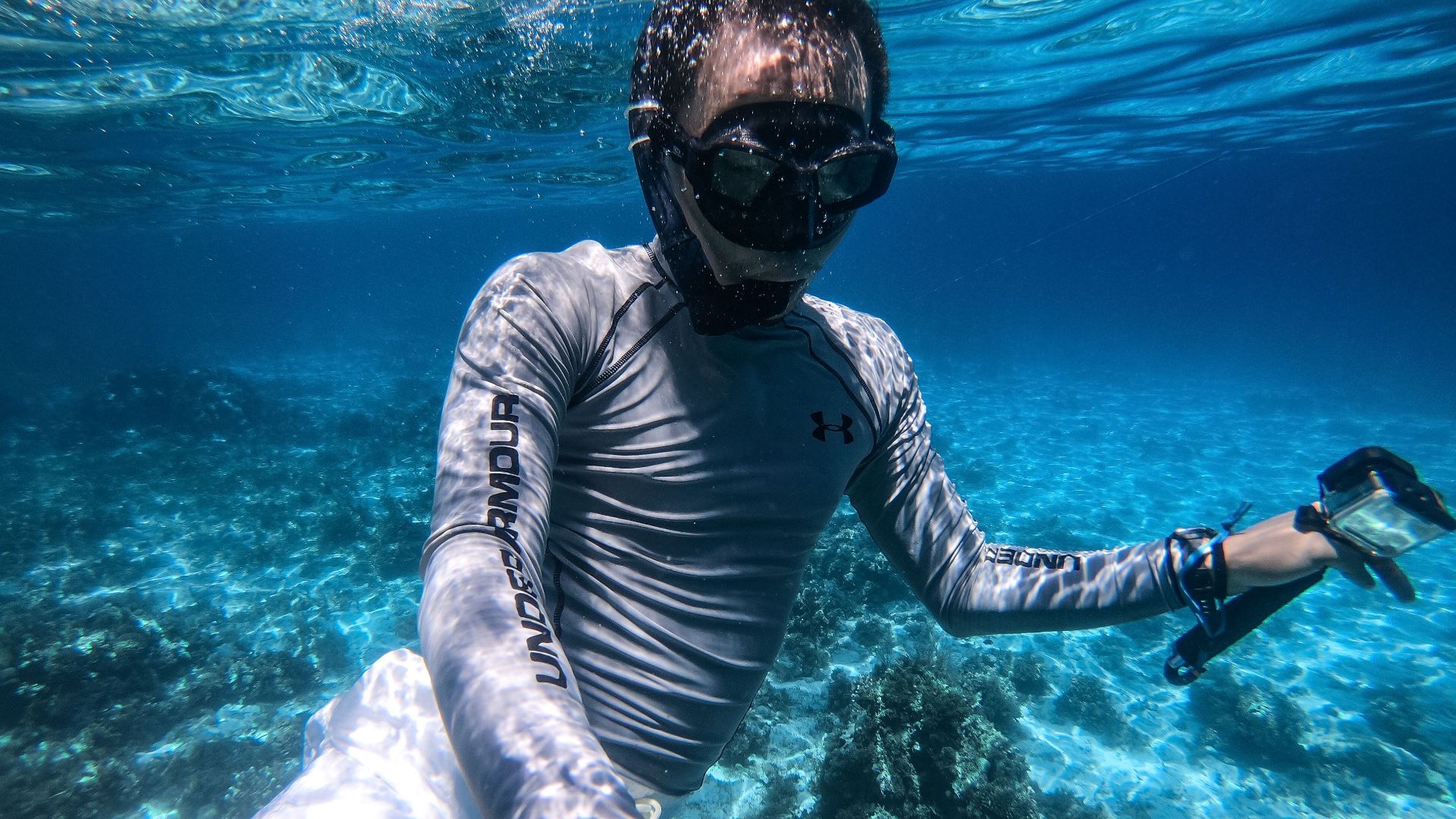 A man snorkeling in crystal clear blue ocean water, surrounded by coral, enjoying an underwater adventure.