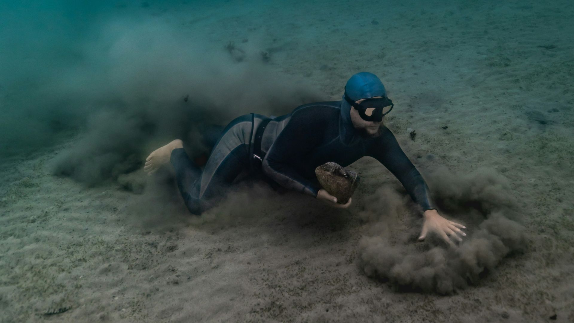 Man free-diving on sandy ocean floor stirring up sediment