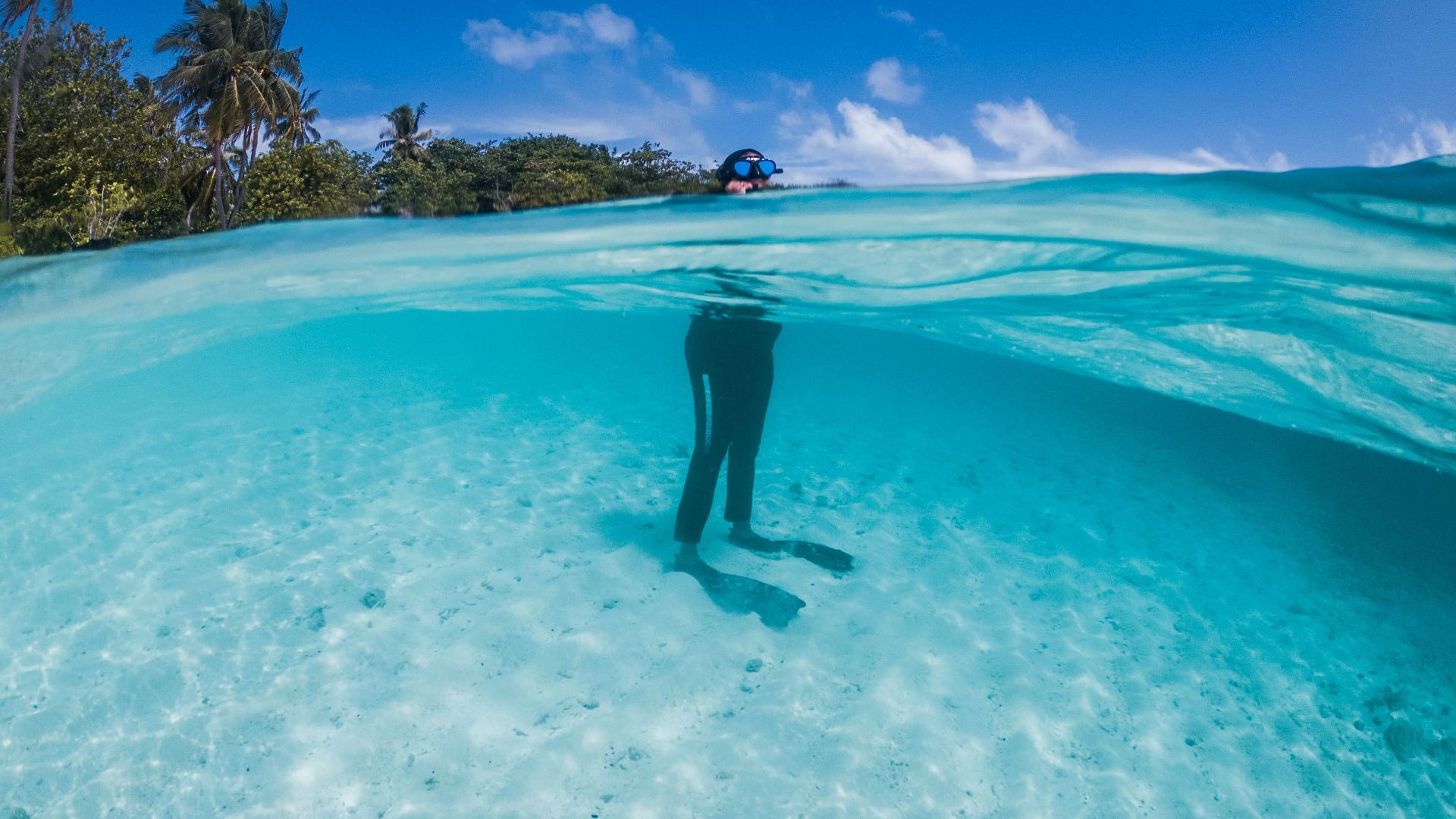 Unrecognizable person in snorkeling mask and goggles standing in transparent blue seawater in tropical nature on sunny clear day