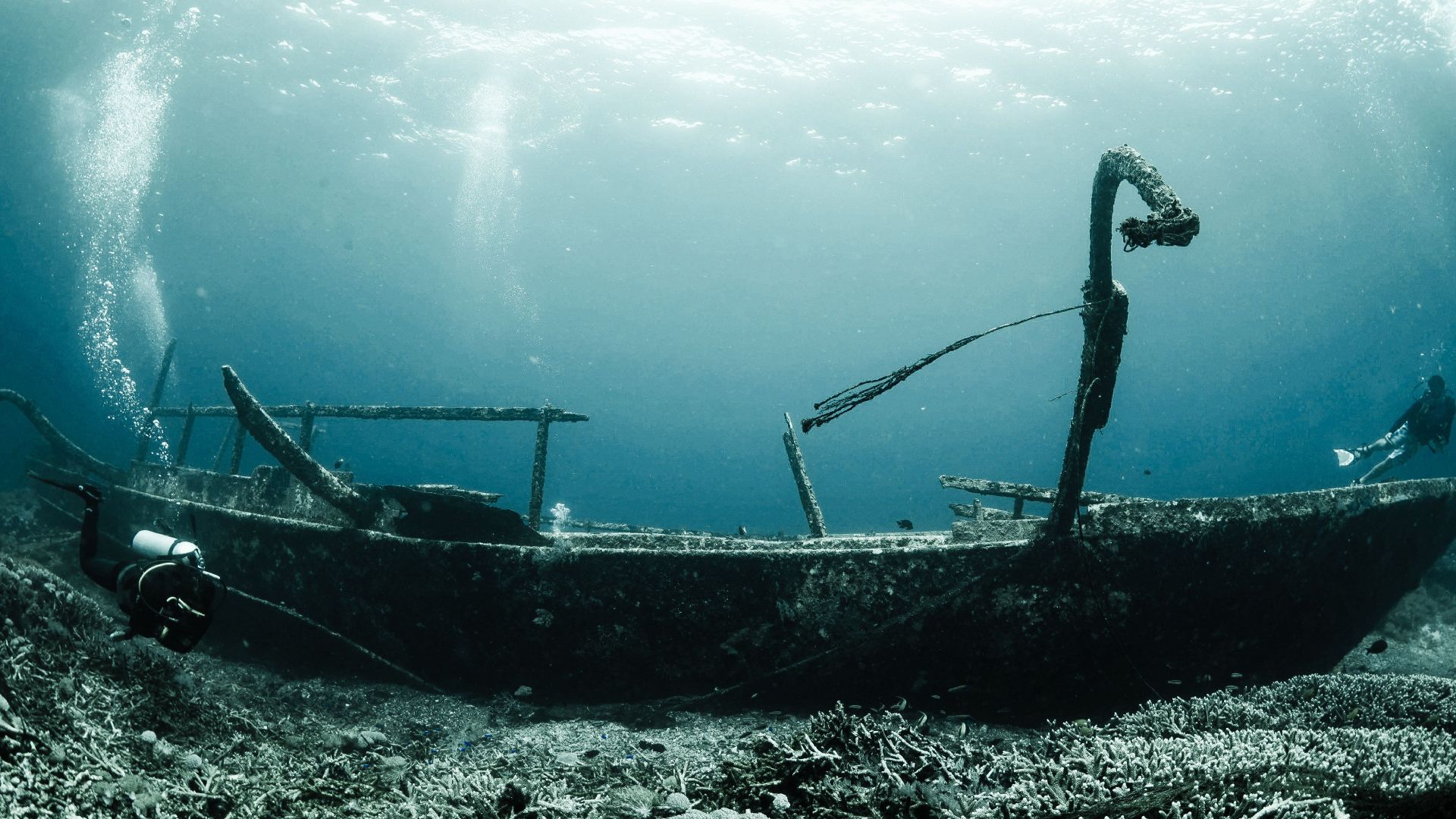 Explore a mysterious shipwreck underwater with scuba divers capturing the serene beauty of the deep blue sea.