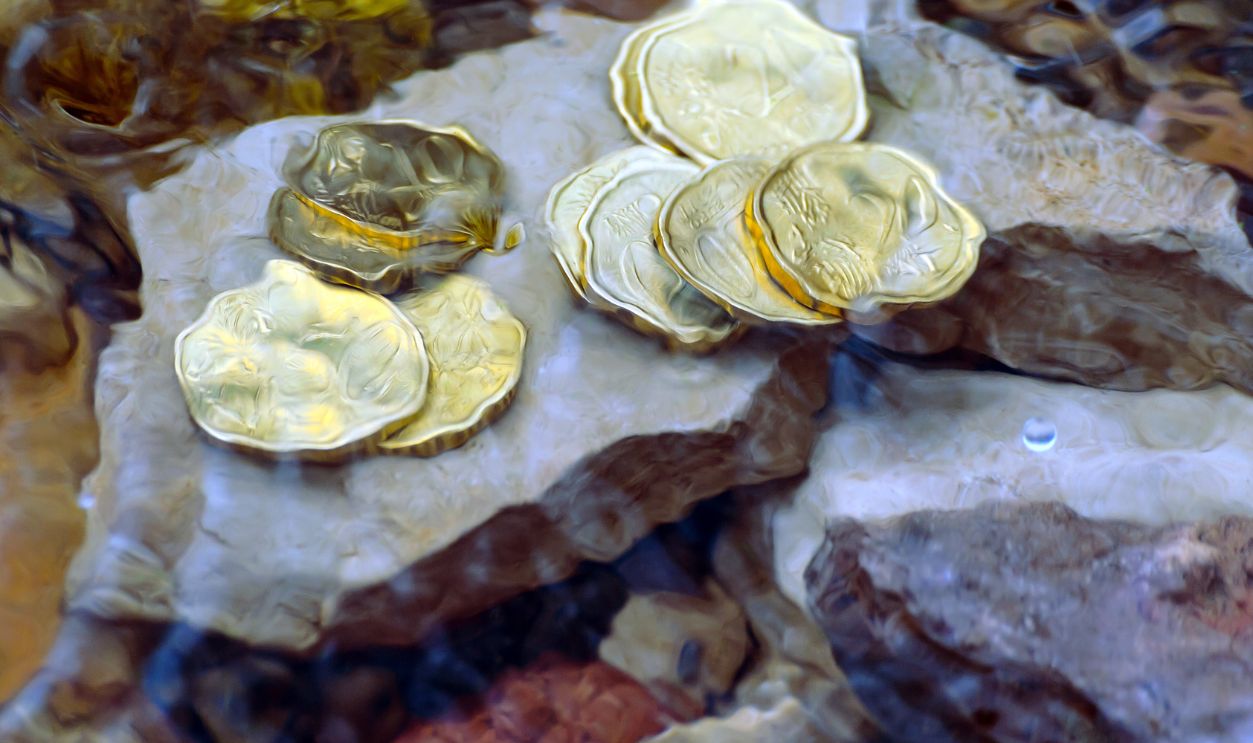 money in the river on the rocks, running out as fast as the water flows, coins under water, waves covered