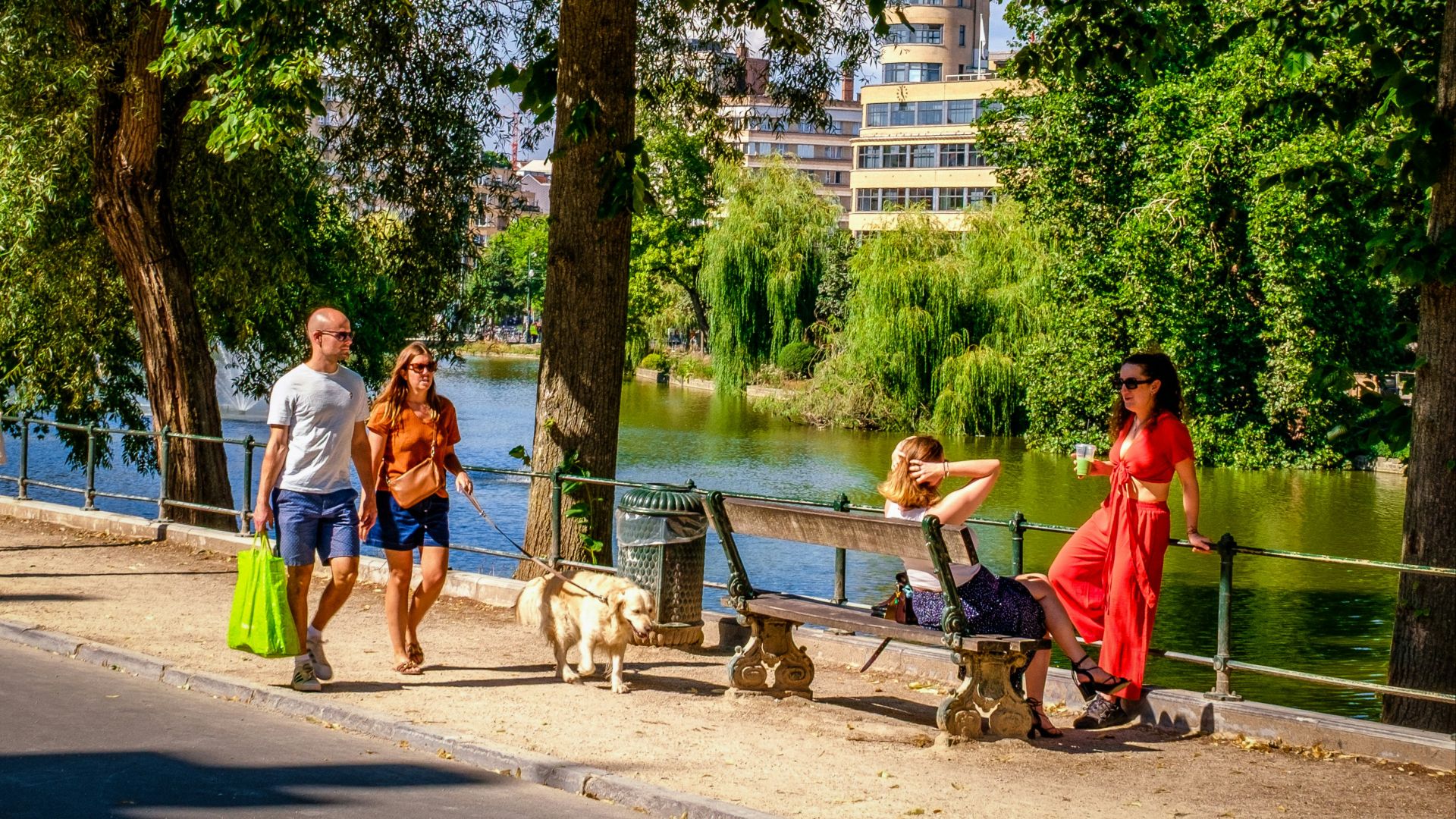 People walking dog by lake with buildings in background
