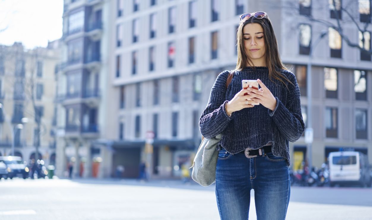 Pensive female traveler in casual clothes dialing number on smartphone calling taxi service during city tour.Young woman checking email on mobile connected to 4g internet standing on advertising area