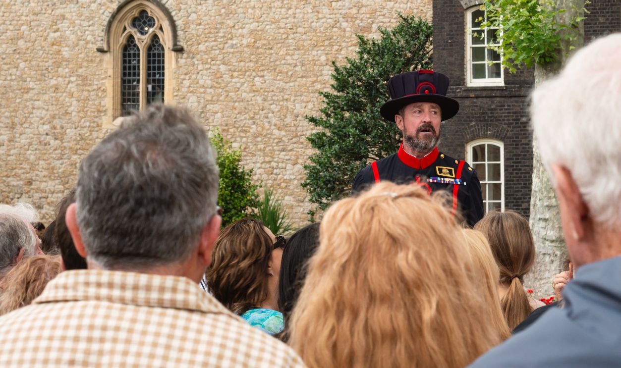 Tower of London, UK, July 25, 2023. A Yeoman Warder, known as a Beefeater, leads a guided tour at the Tower of London. Historic British tradition with tourists listening attentively.