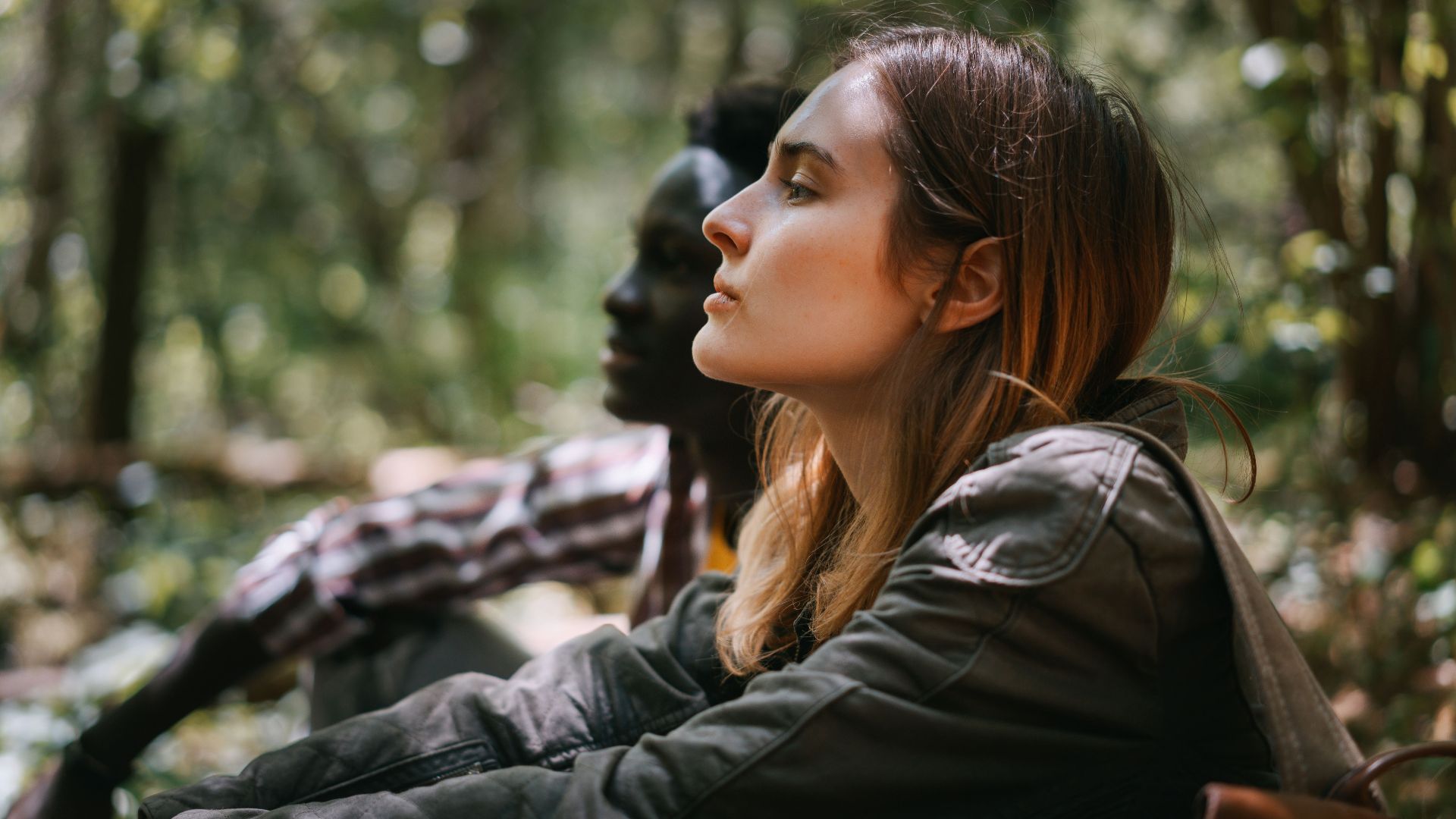Two individuals in a serene forest, facing nature, enjoying tranquility.