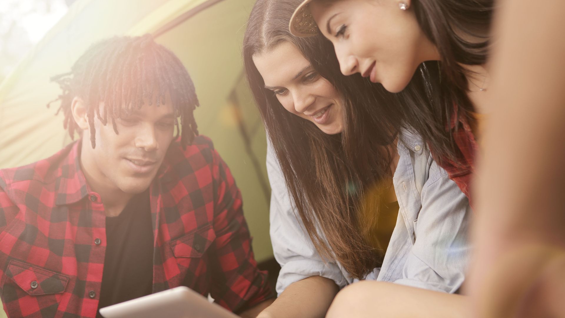 Group of young adults enjoying leisure time camping and watching something on a tablet.