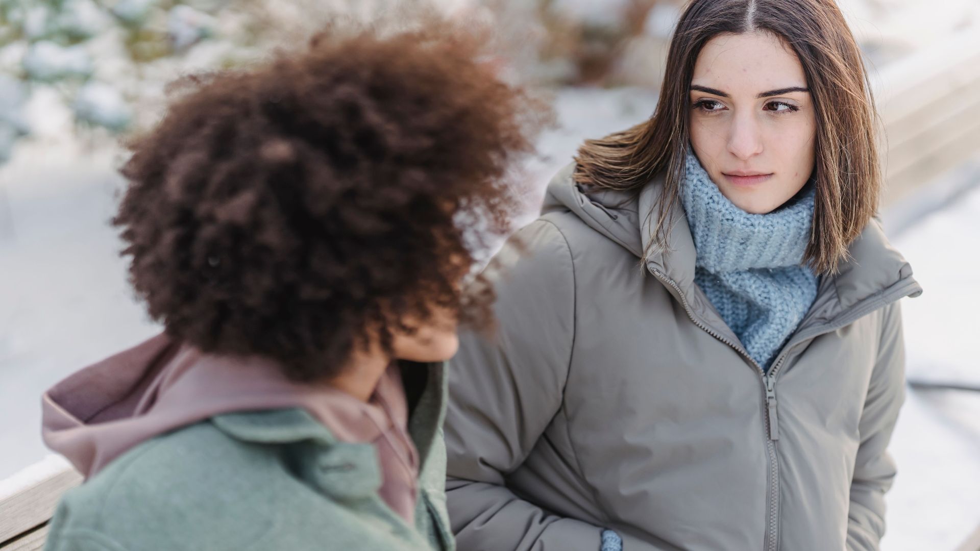 High angle of crop female listening to friend while sitting on wooden bench in winter park