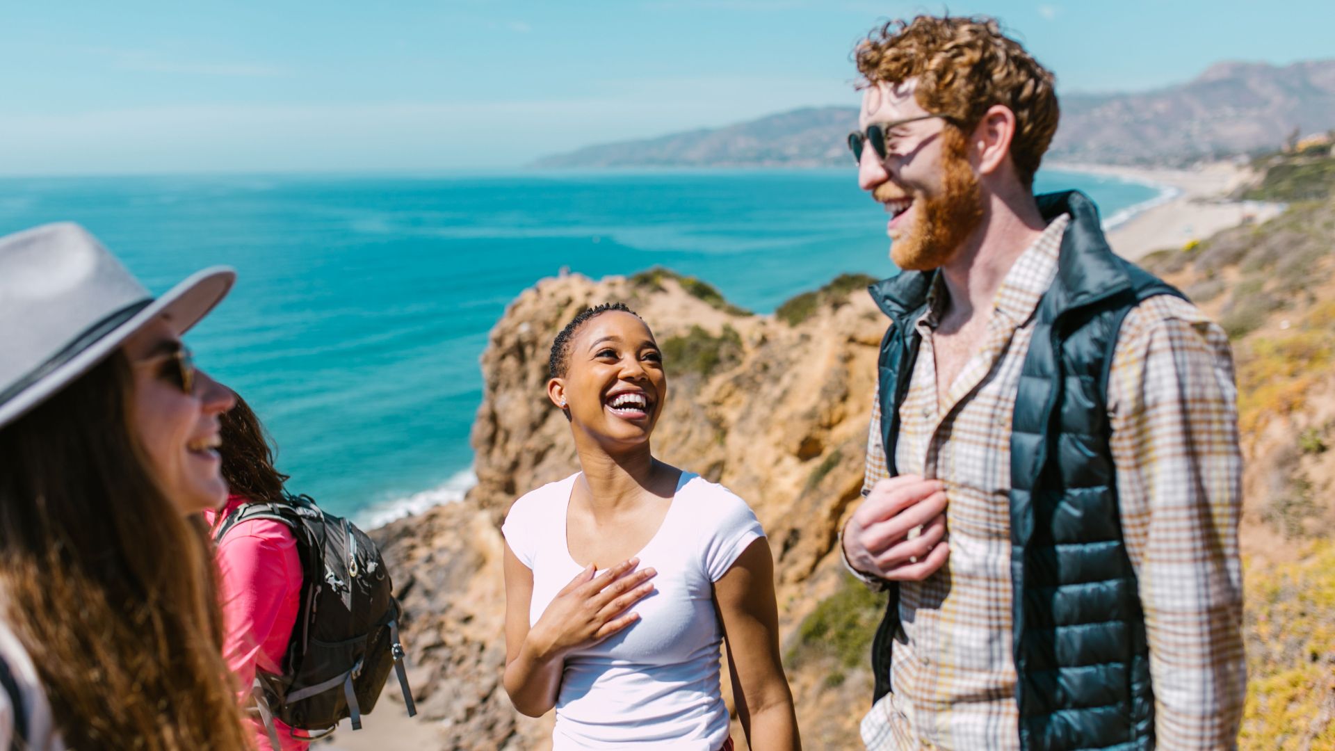 Joyful friends exploring a picturesque coastal trail under the sunny sky.