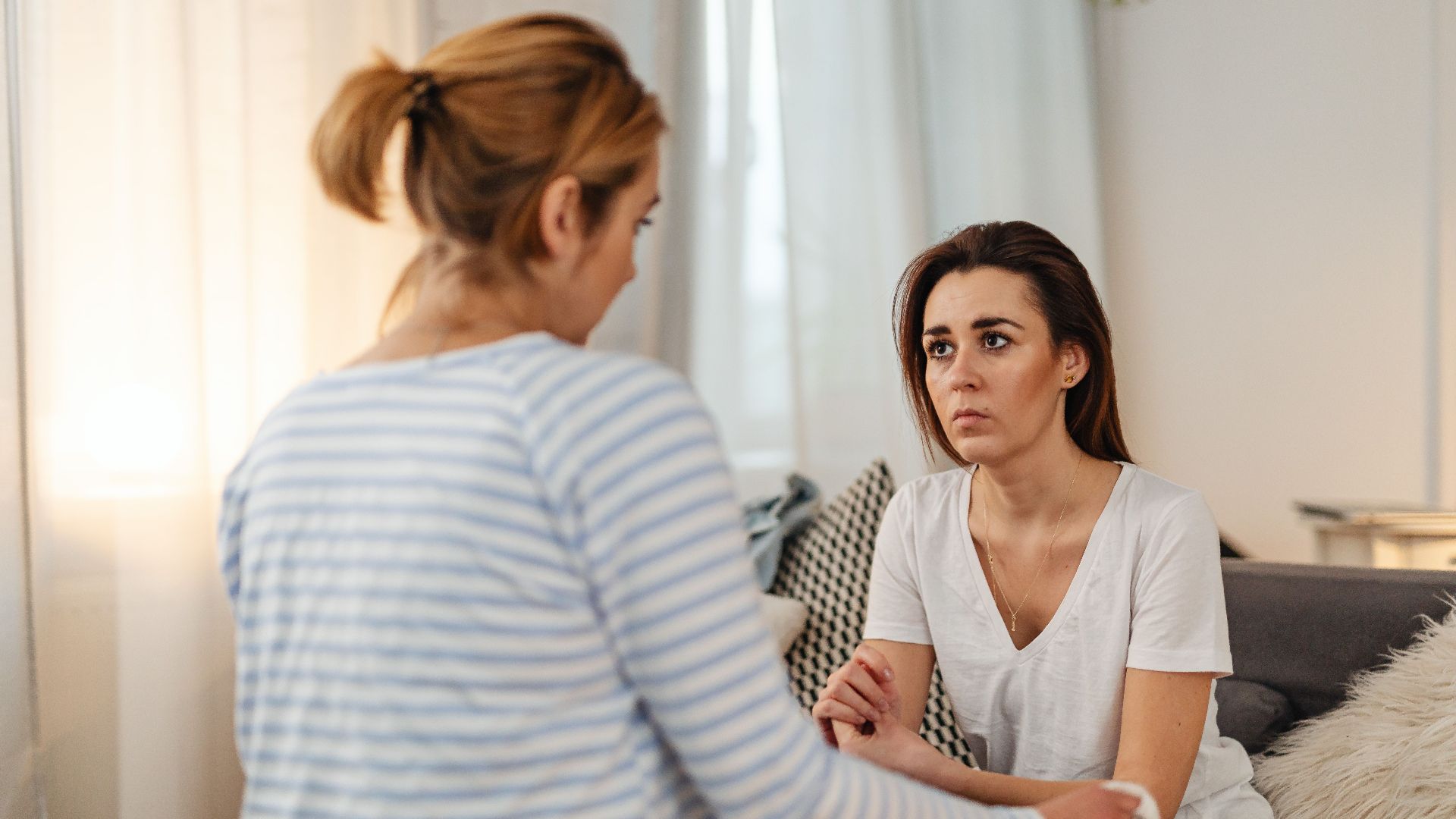 Two women engaged in a serious conversation, sitting indoors with a blurred background.